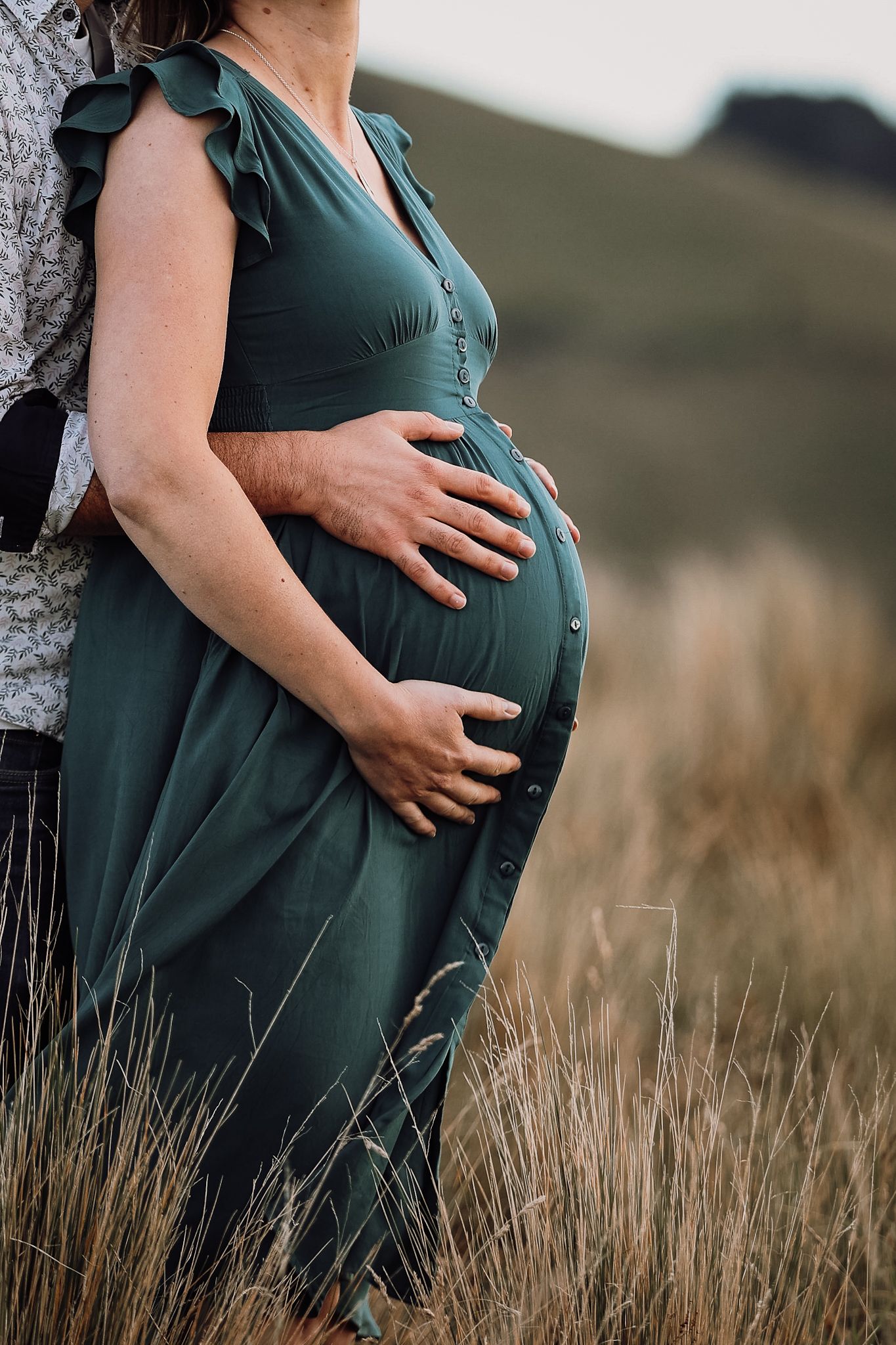 Close up of a pregnant woman’s stomach with partners hands on top during a maternity photoshoot