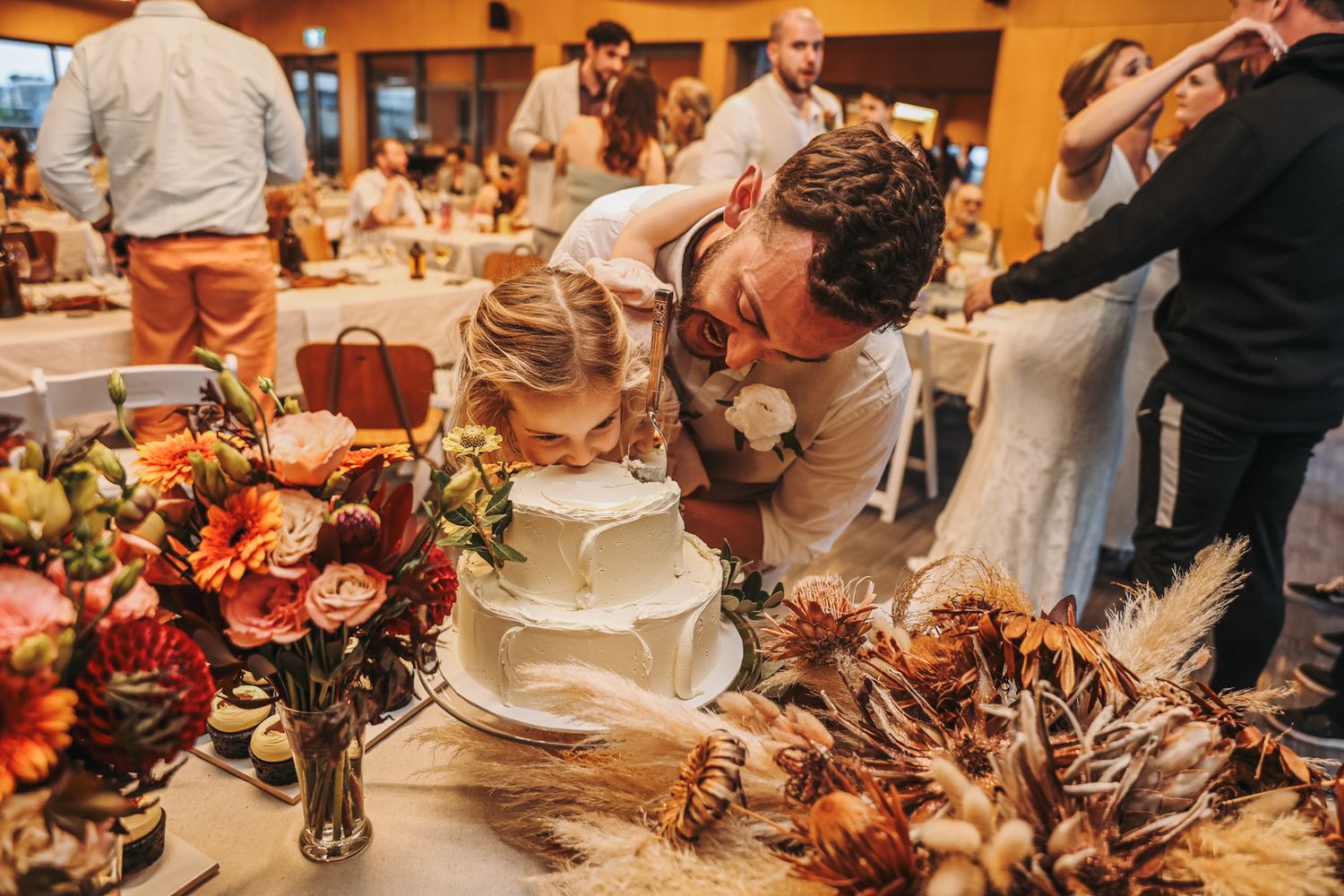 Groom holds his young daughter up as she takes a bite of wedding cake straight from the top layer