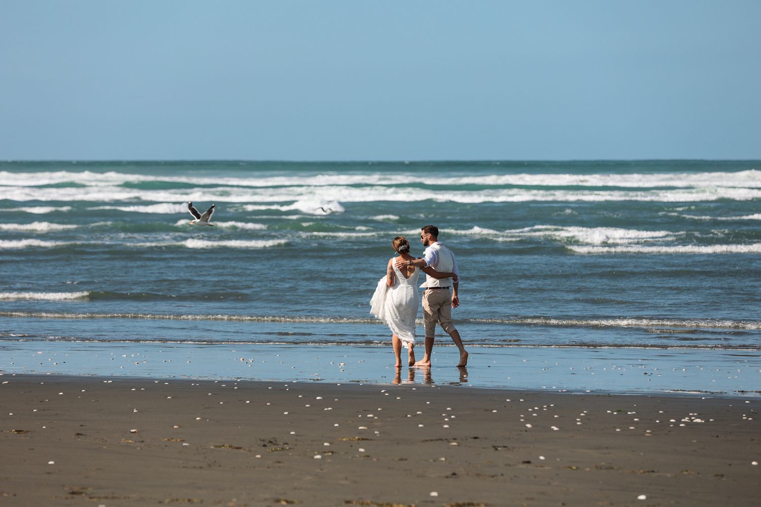 Bride and groom walking barefoot in the surf at Southshore New Brighton Beach during their newlywed portraits