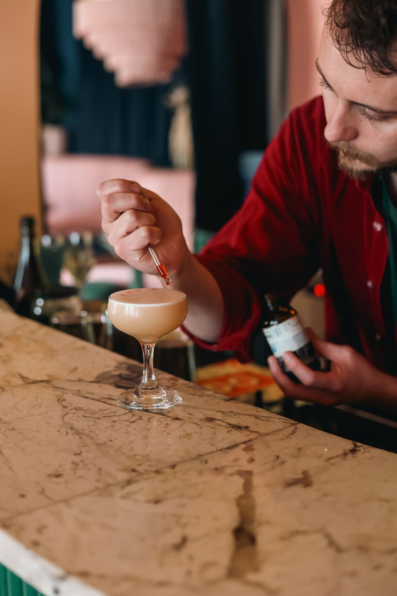 Bartender dropping Peychaud bitter droplets onto a gin sour cocktail