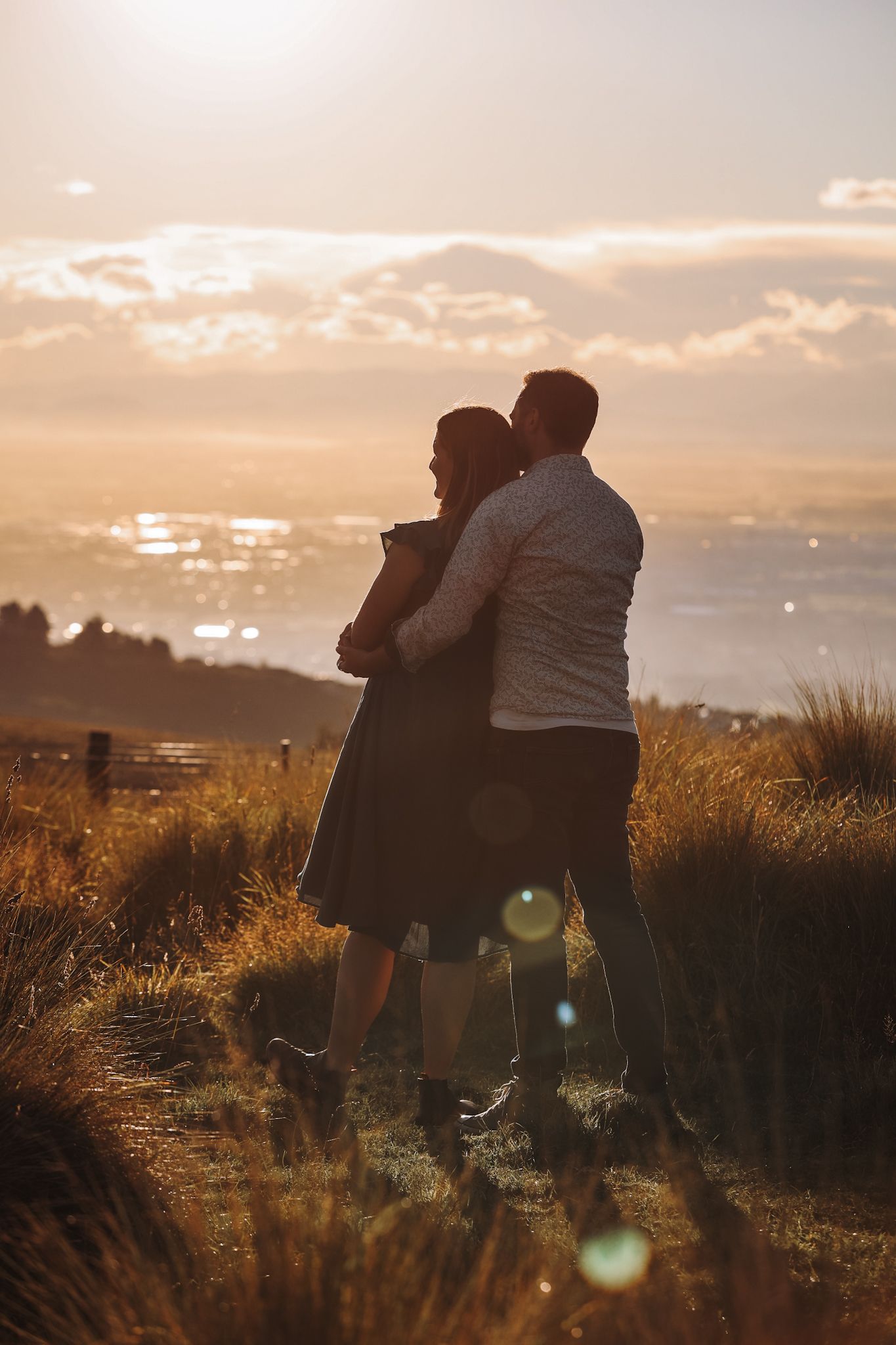 Lens flare peeking through the clouds in front of an expecting couple during their maternity photoshoot While they face away from the camera