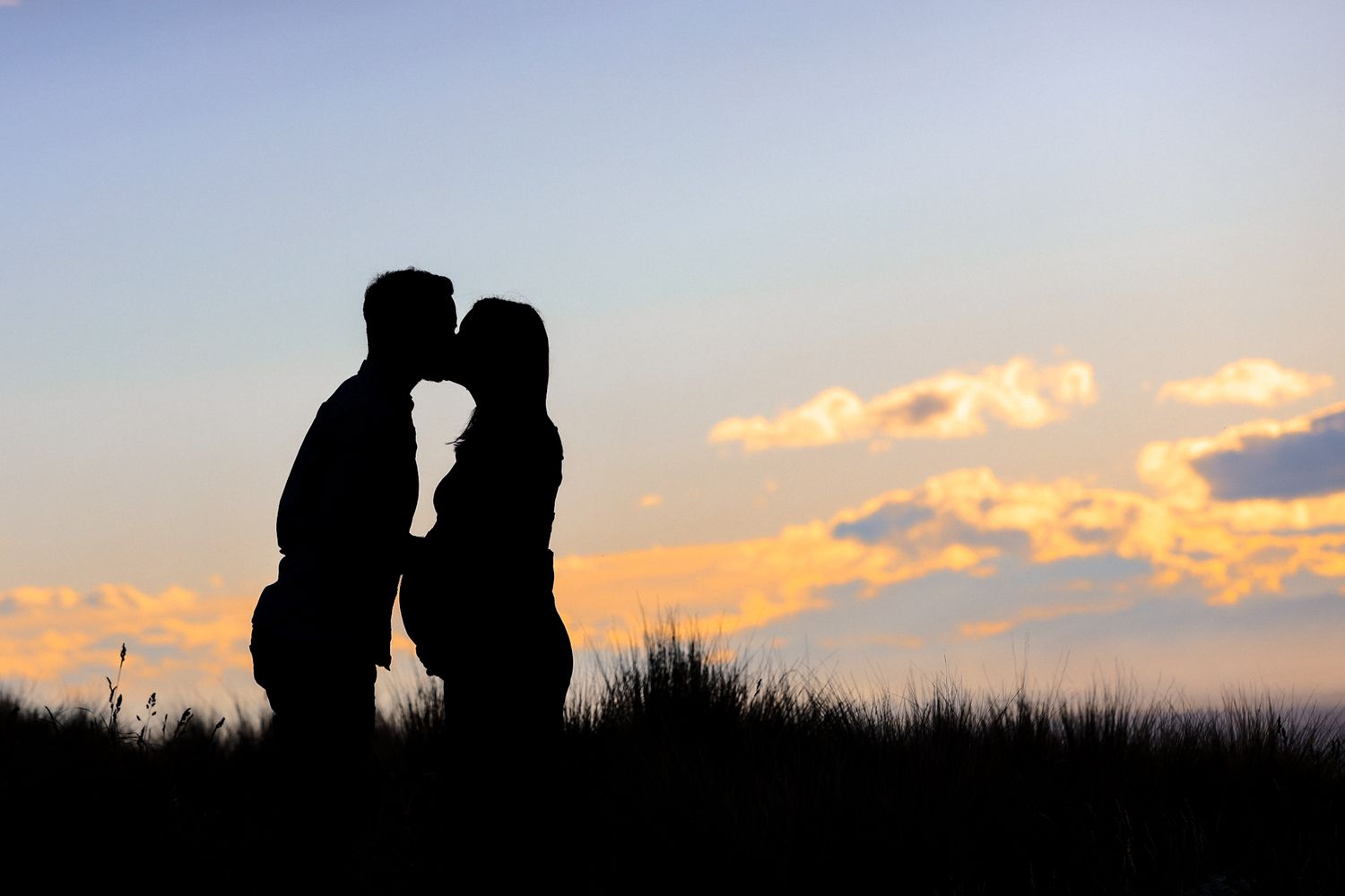Silhouette of an expecting couple kissing against a vibrant sunset