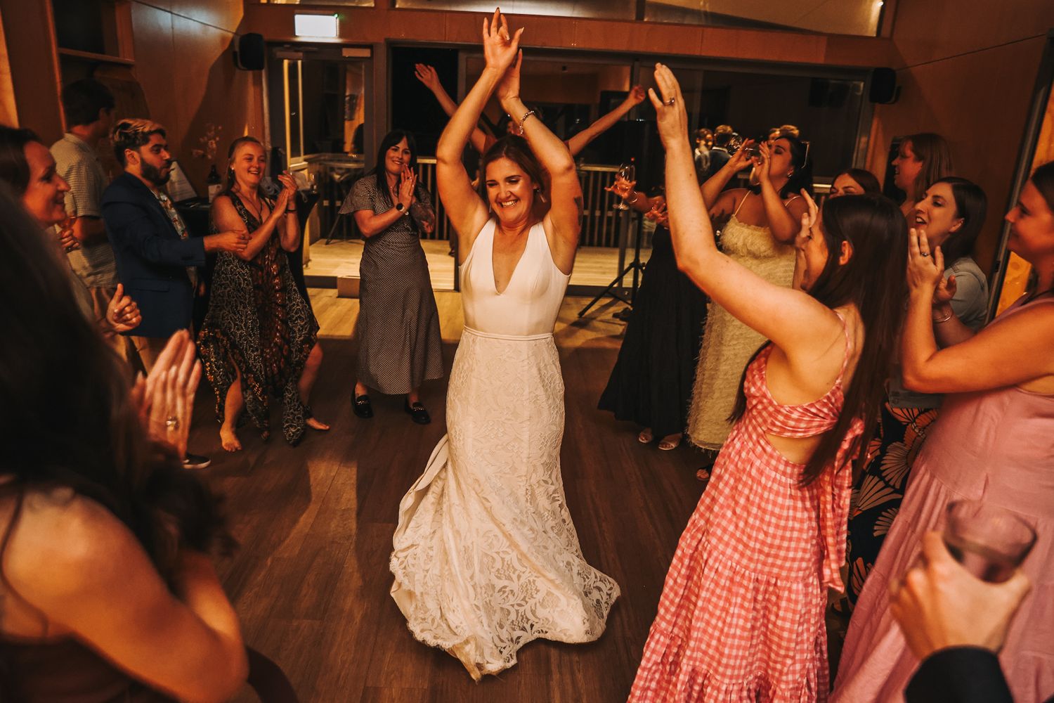 Bride in the middle of a dance circle at her wedding. Guests all raise hands and clap for her.