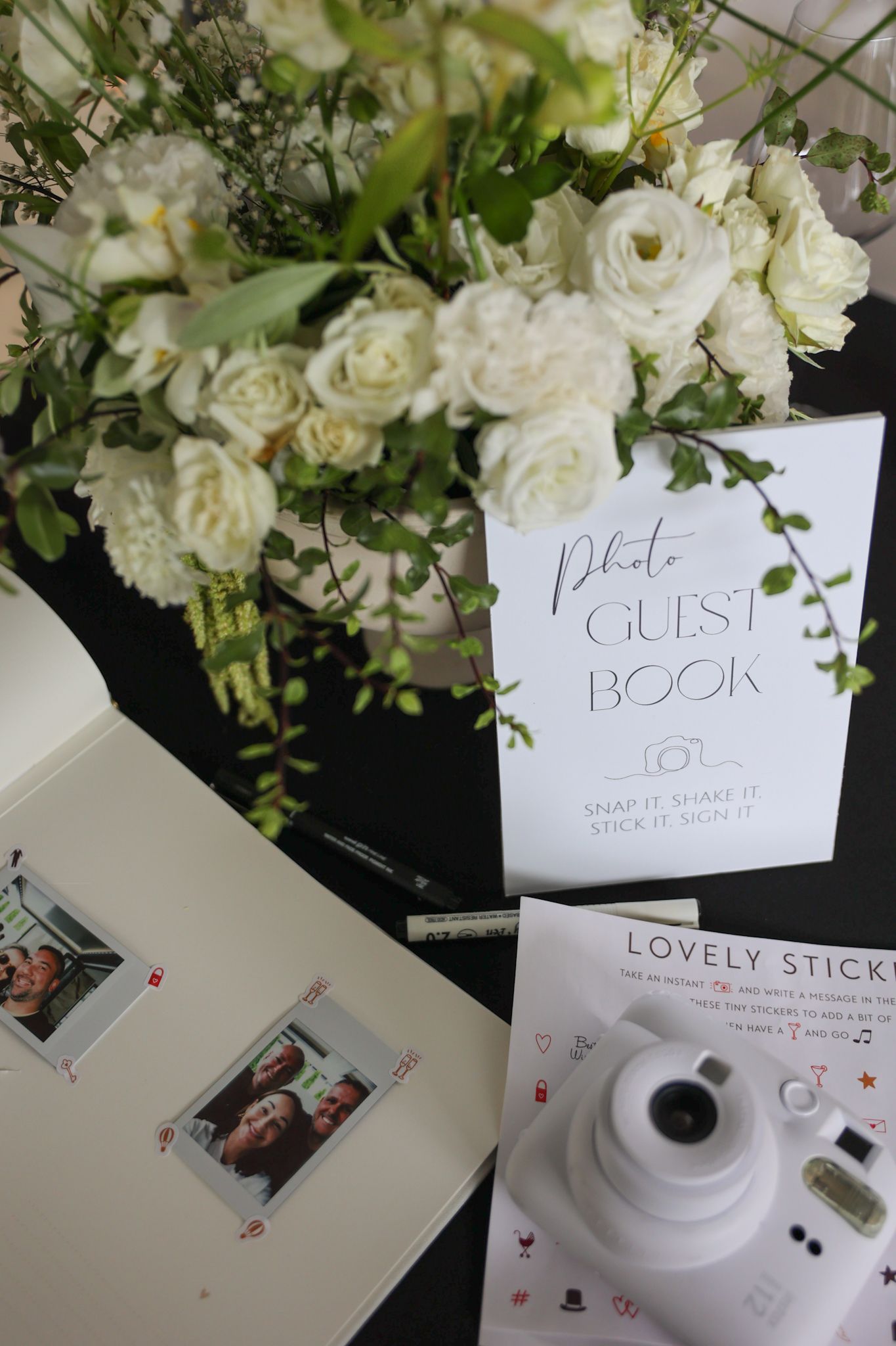 A detail photo of a wedding party and a photo guest book. A Polaroid camera, some flowers, and a notebook for guests to write in.