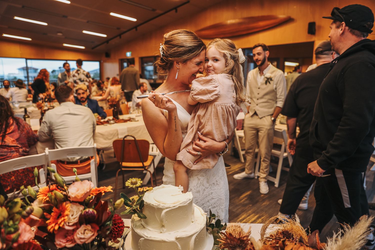 Bride holding her young daughter while they share a piece of wedding cake