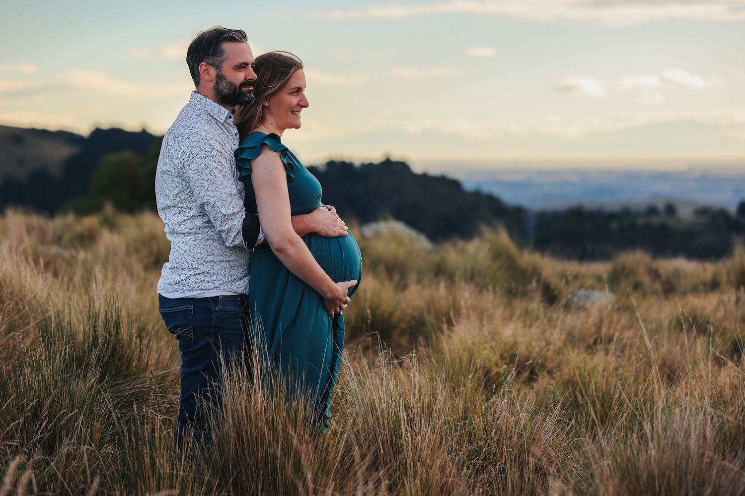 Expecting couple during a maternity photoshoot looking out onto christchurch city from the Port Hills