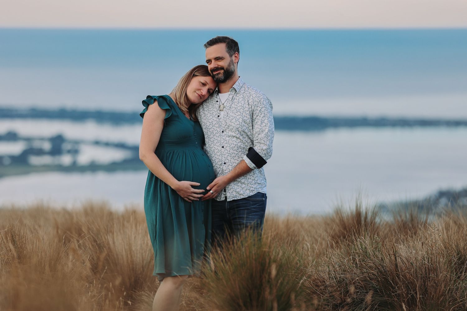 Expecting couple during a maternity photoshoot against a view of the ocean from the christchurch port hills.