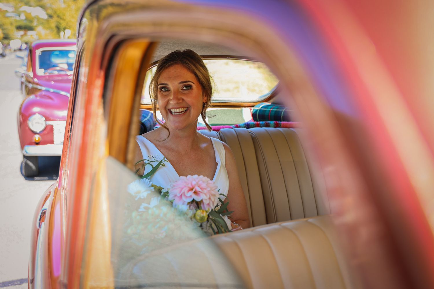 Bride caught through the window of the classic car, smiling in anticipation.