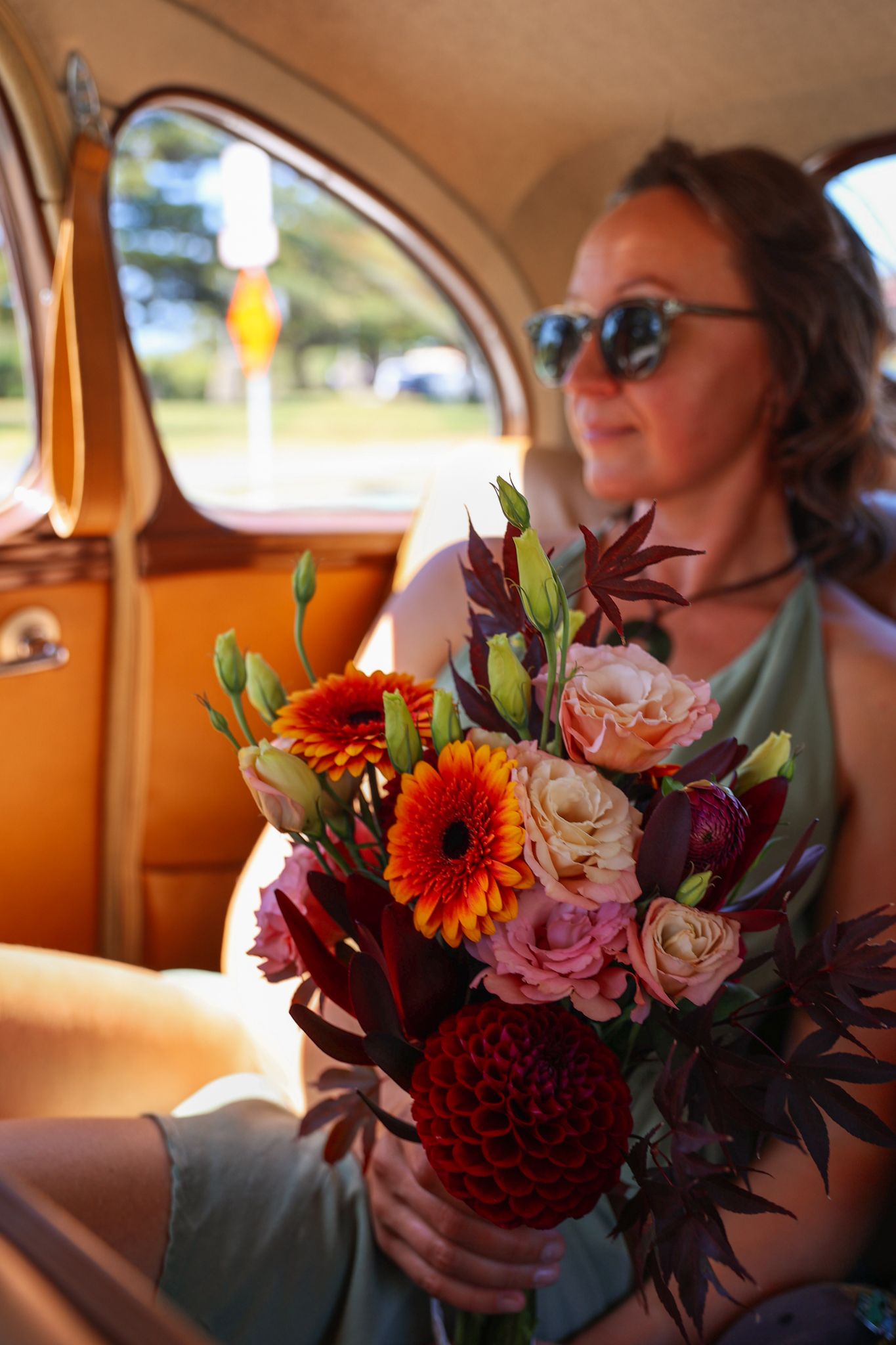 Bridesmaid holding a bouquet of flowers from inside the classic car on the way to the wedding.