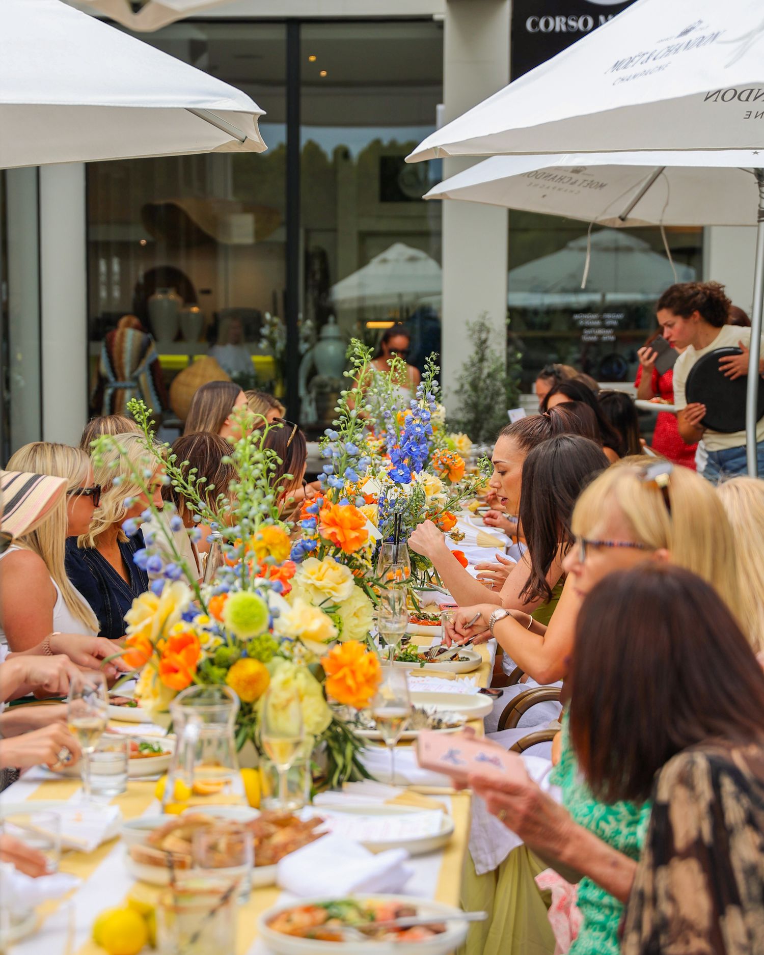 A birthday summer garden party in the courtyard at Brigitte’s Merivale. Ladies sat at a long table with colorful flowers.