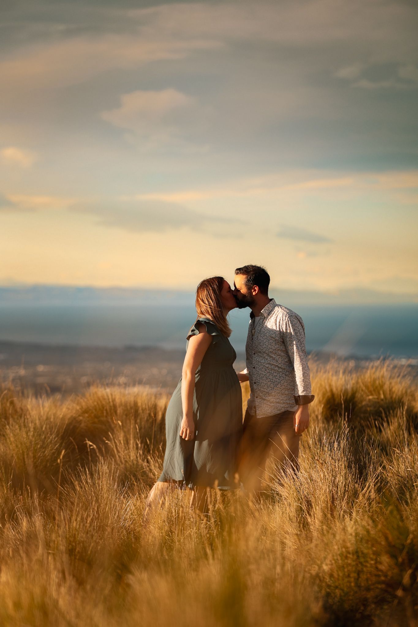 Dreamy couple kissing in the long grass at golden hour in the christchurch port hills