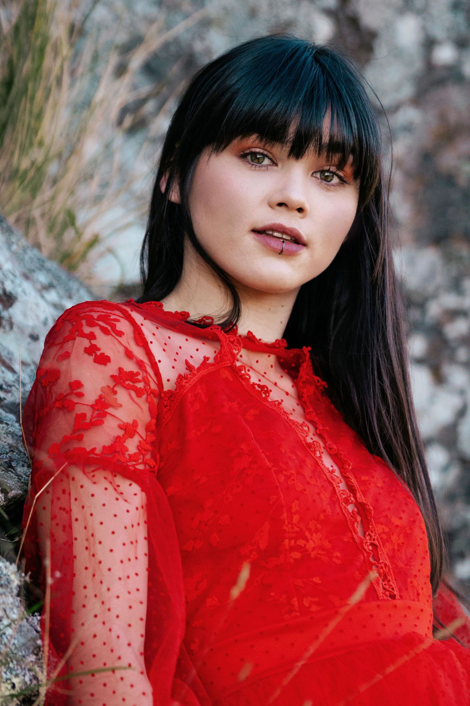 Model in a red dress posing against a rock face during a portfolio photoshoot