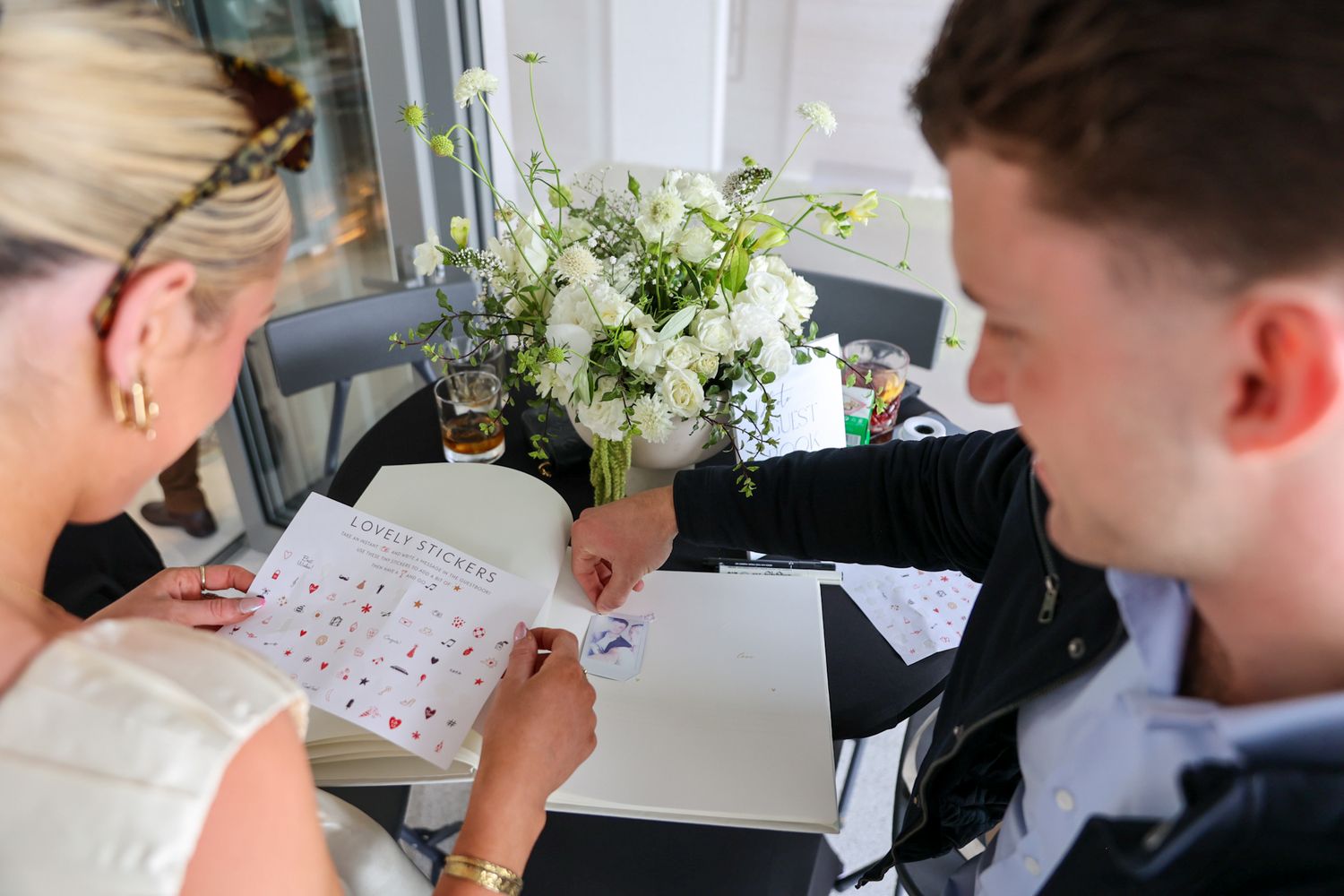 Guests at a party writing in a guest book, sharing a Polaroid photo that they have just taken of themselves.