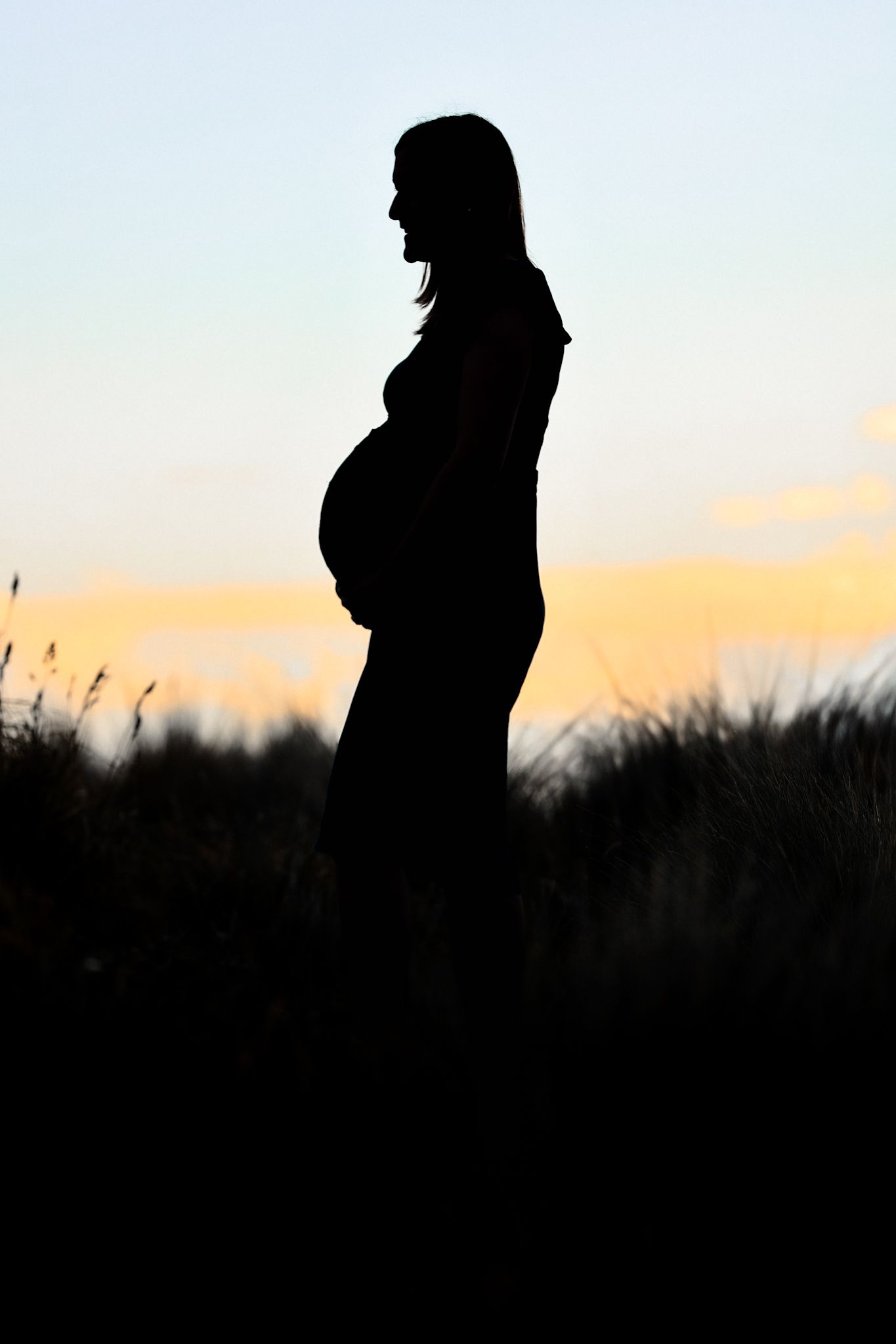 Silhouette of a pregnant lady with the sunset behind her during her maternity shoot