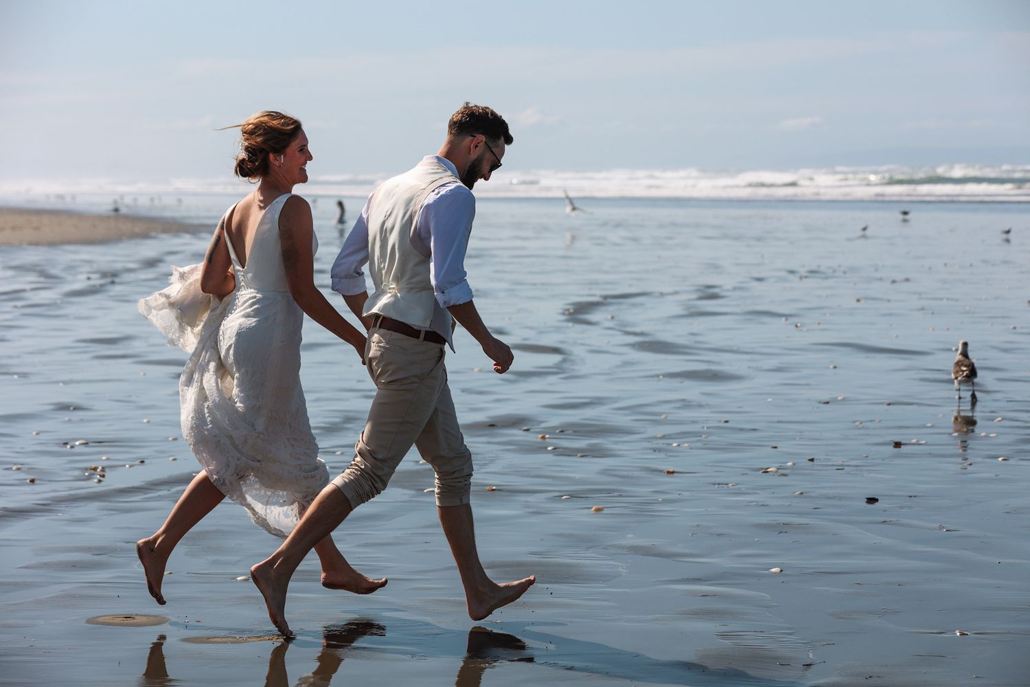 Bride and groom running barefoot in the surf at Southshore New Brighton Beach during their newlywed portraits