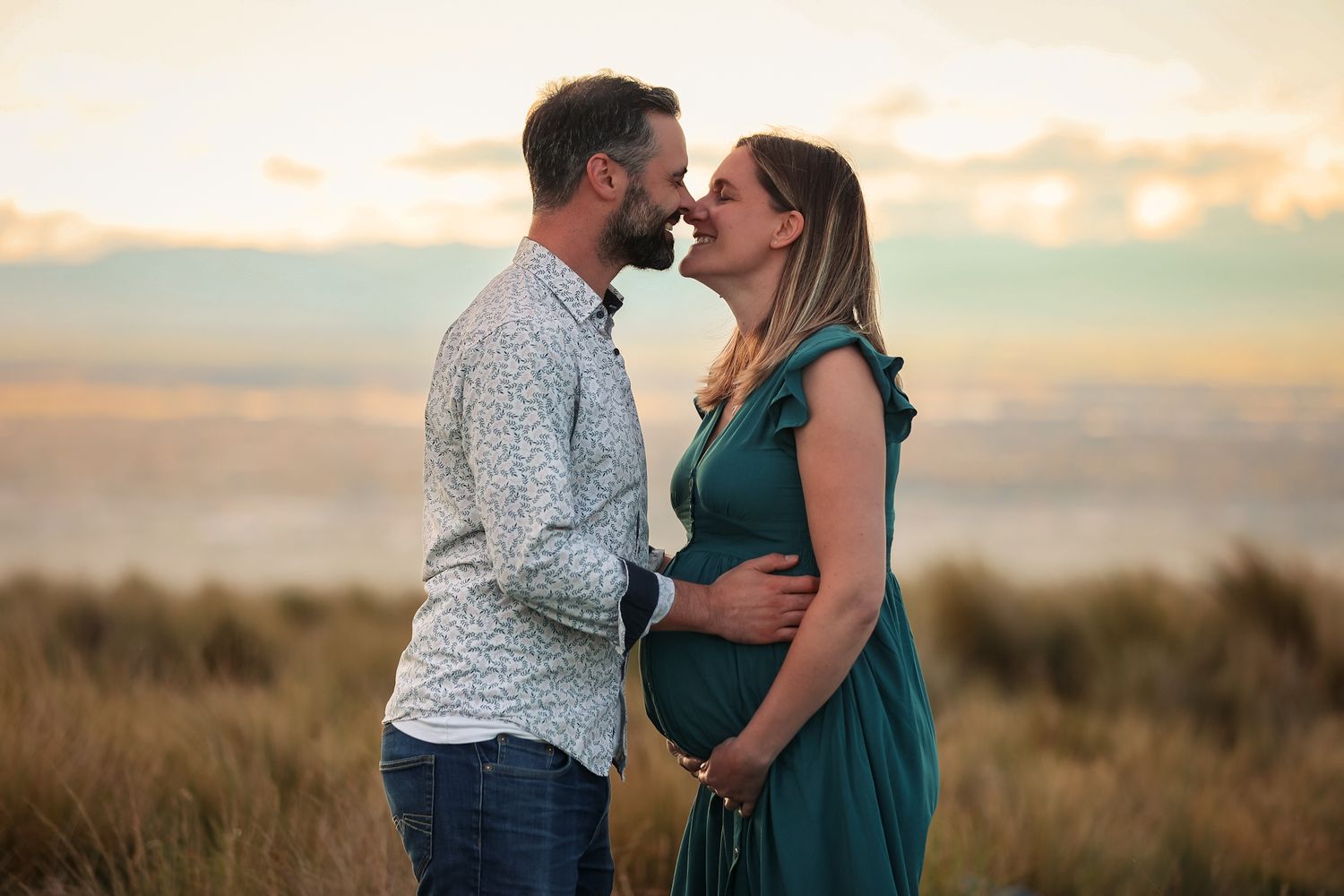 Expecting couple kissing against a city scape and sunset on the Christchurch Port Hills