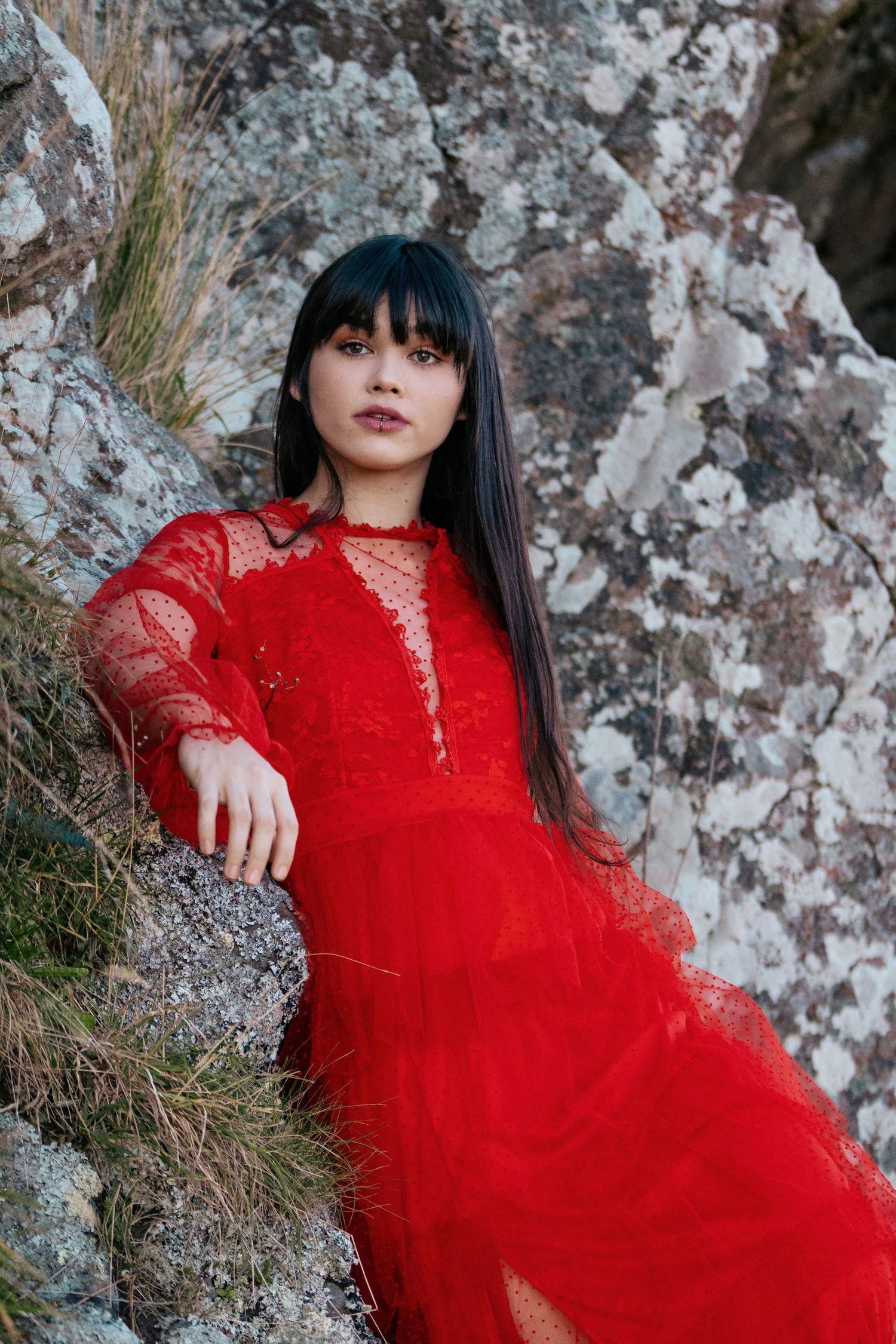 Model in a red dress posing against a rock face during a portfolio photoshoot