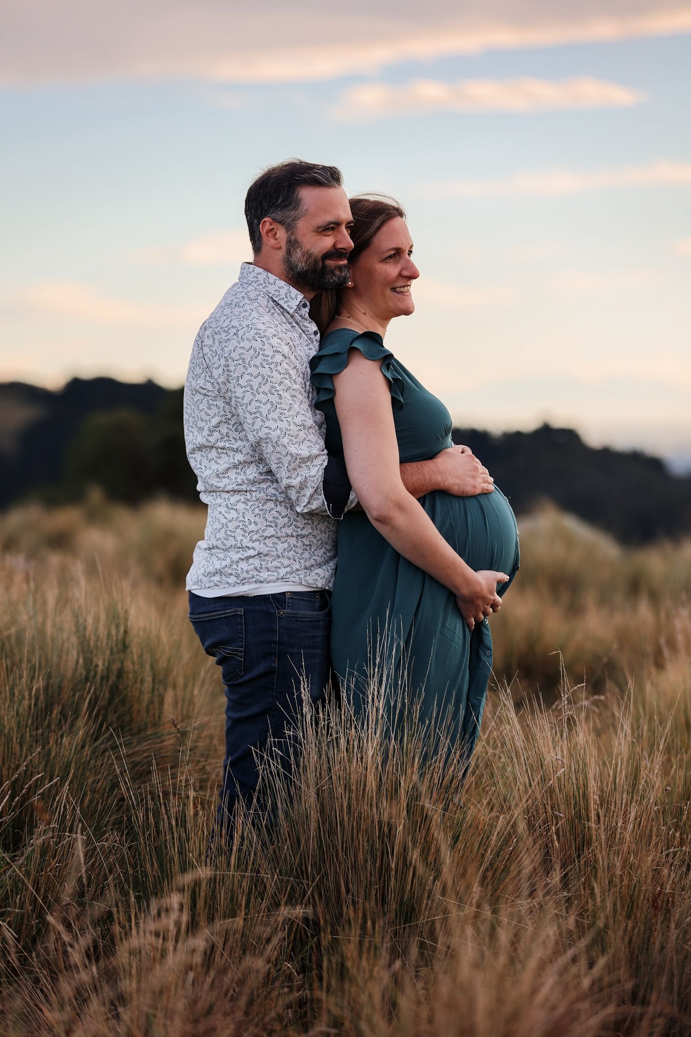 Expecting couple during a maternity photoshoot looking out onto christchurch city from the Port Hills