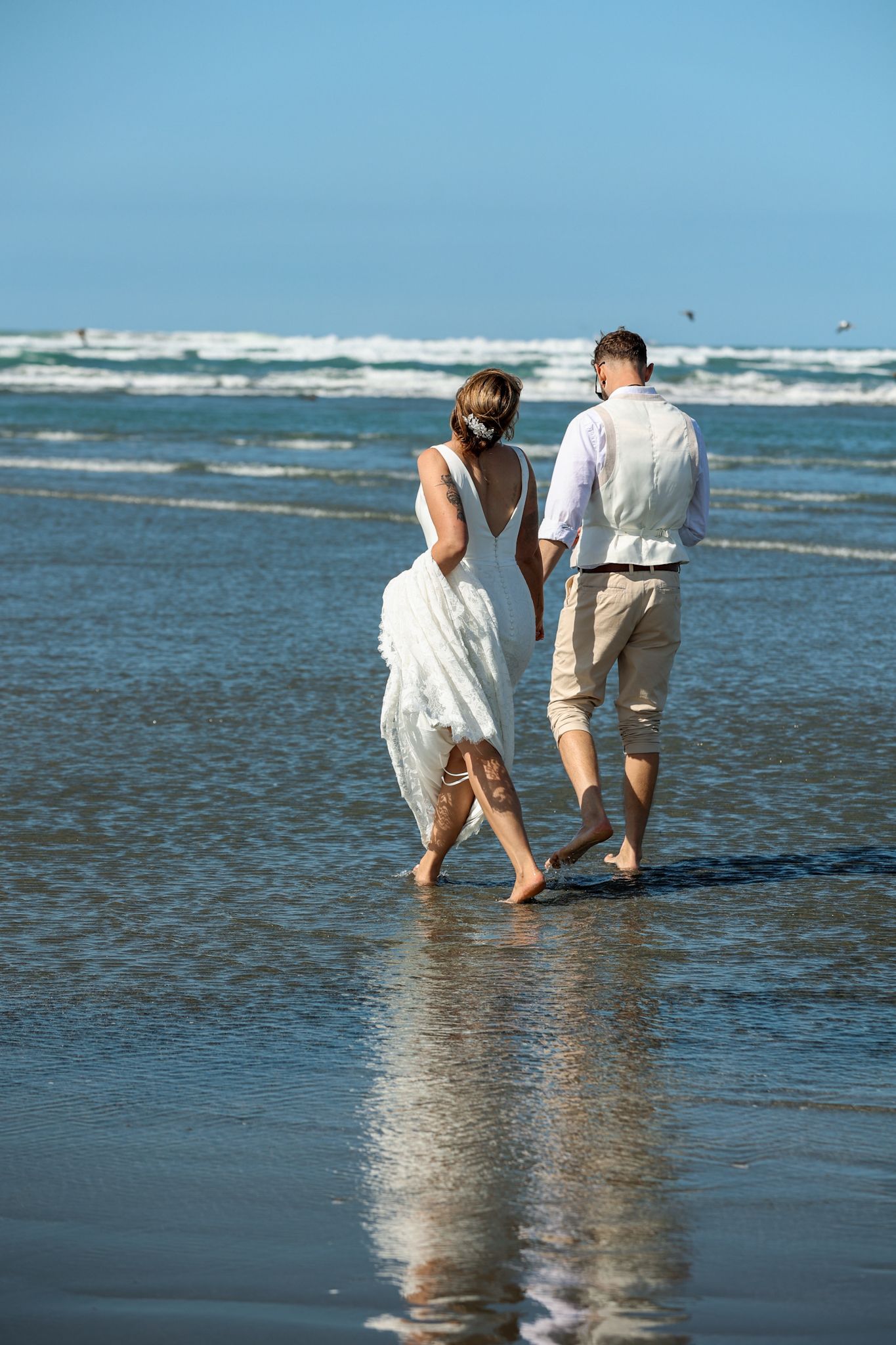 Bride and groom walking barefoot in the surf at Southshore New Brighton Beach during their newlywed portraits