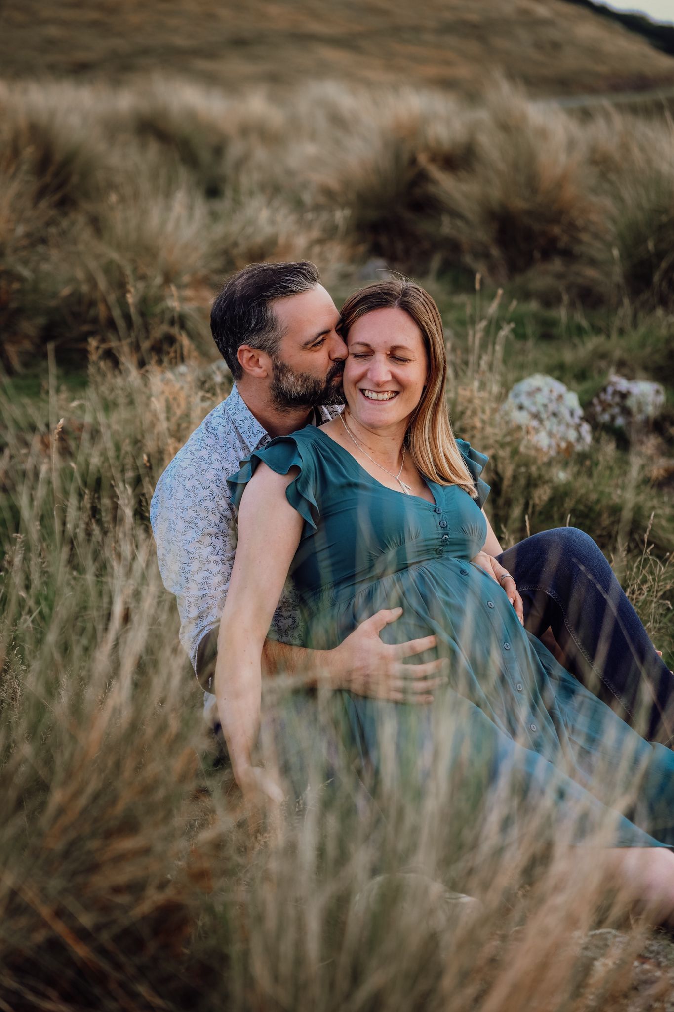 Expecting couple sitting in the long grass during their maternity photoshoot