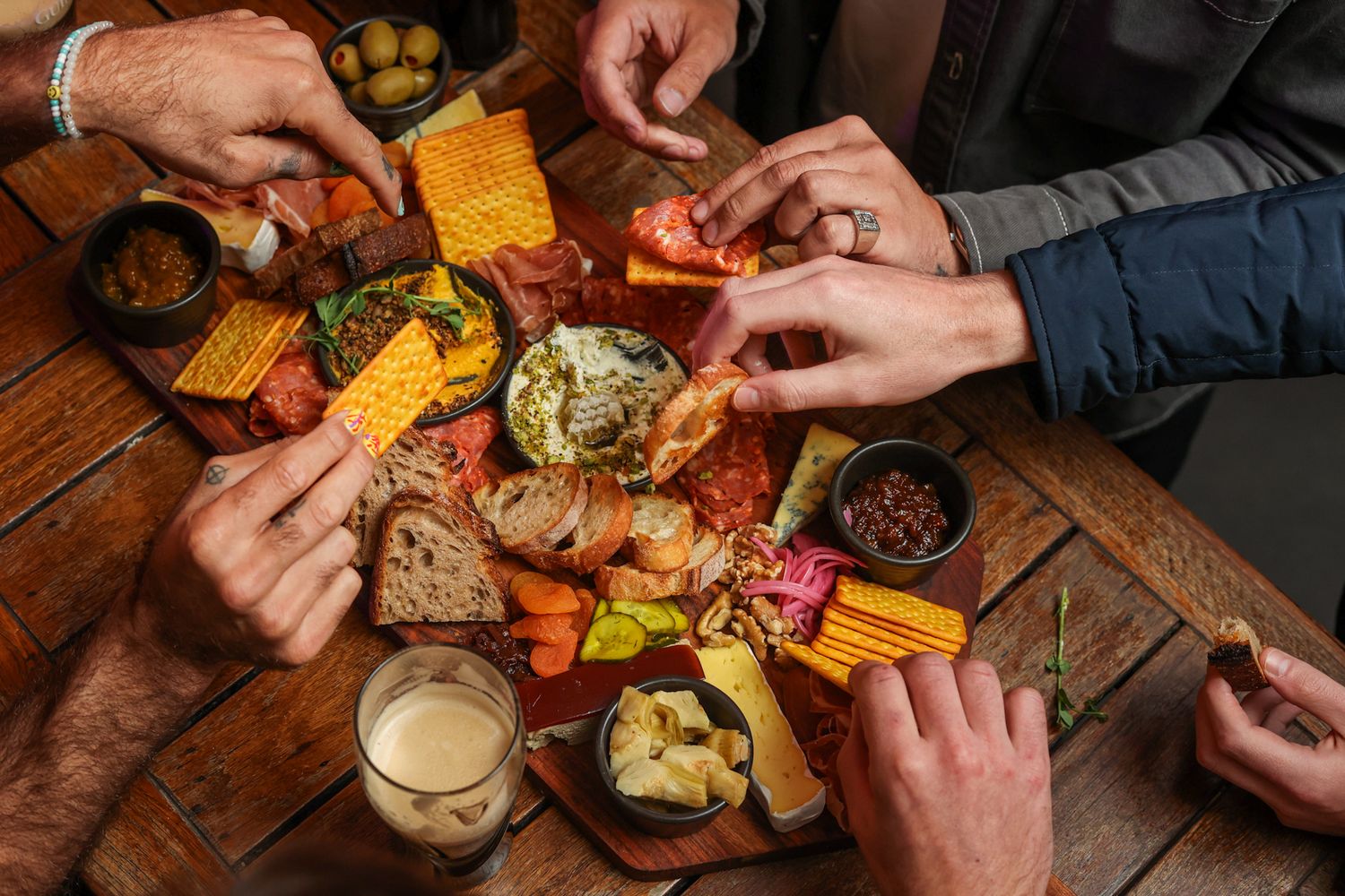 Hands digging into a charcuterie board spread at Aikmans Merivale