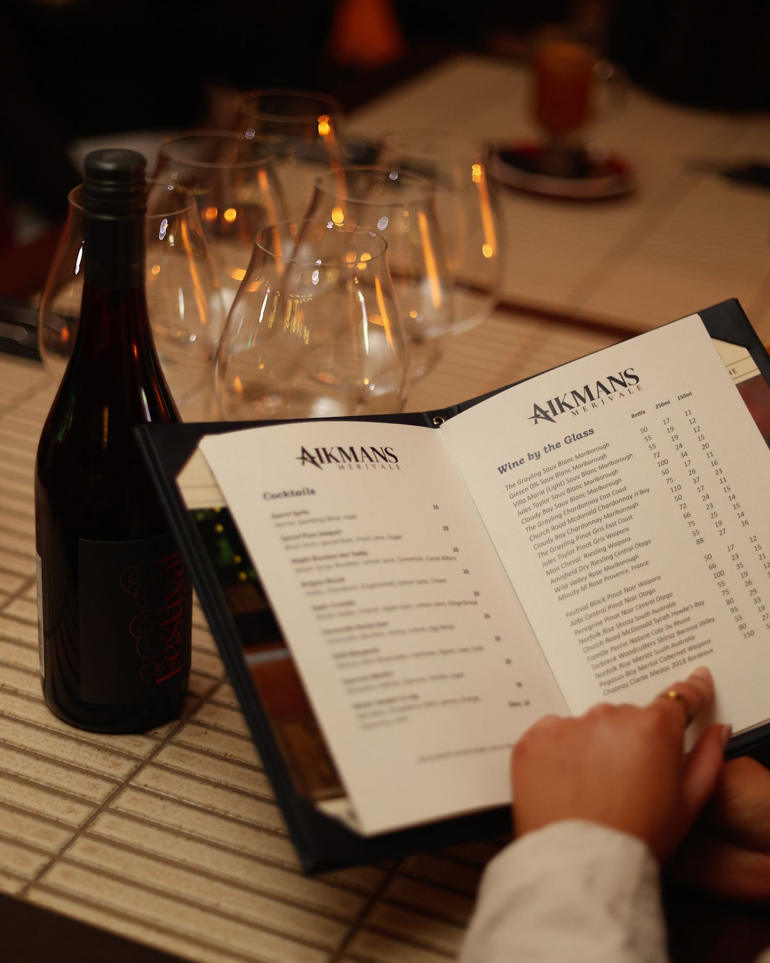 Reading a drinks menu at Aikmans Merivale with a bottle of red wine