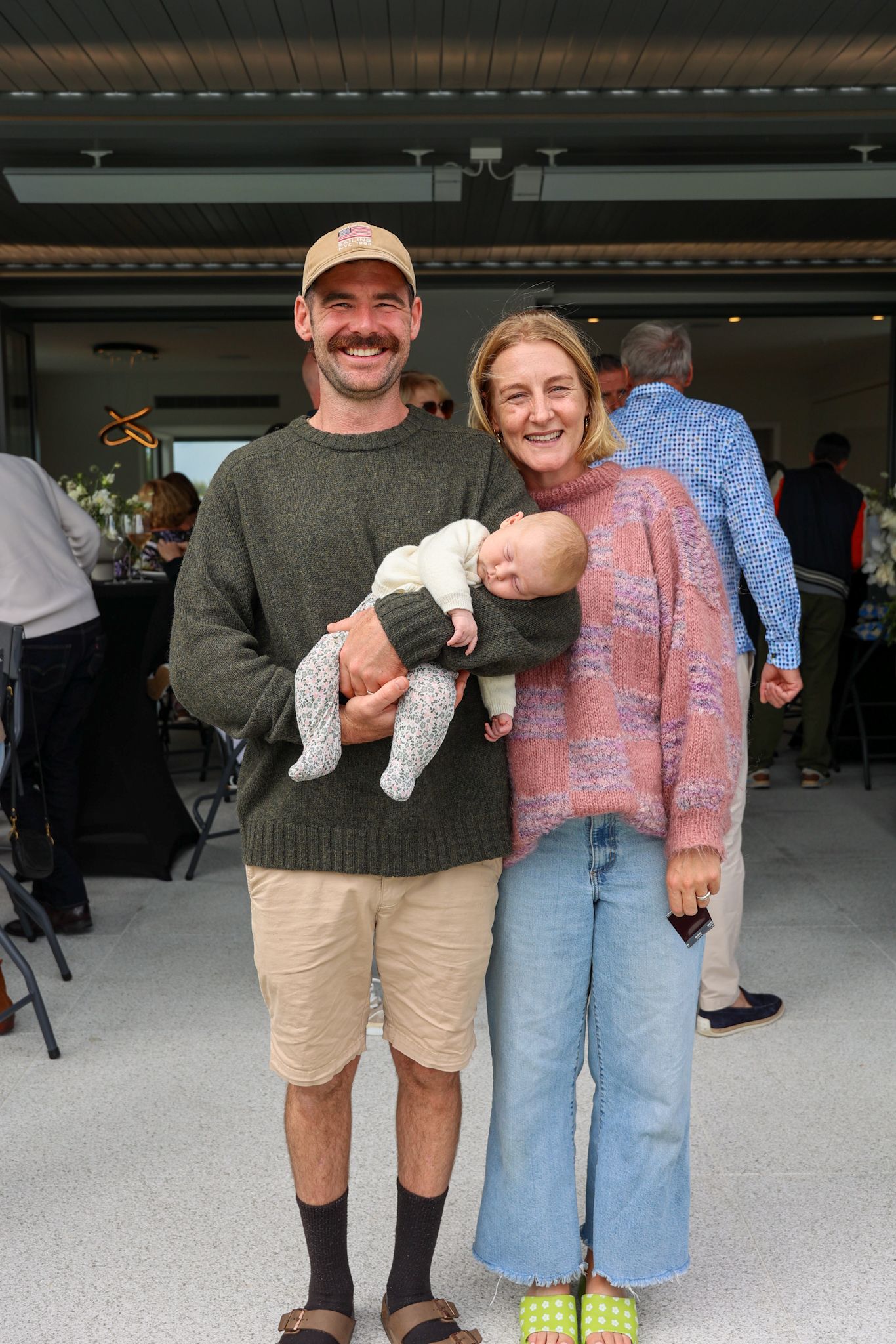 A couple and their newborn having their photo taken at a party.