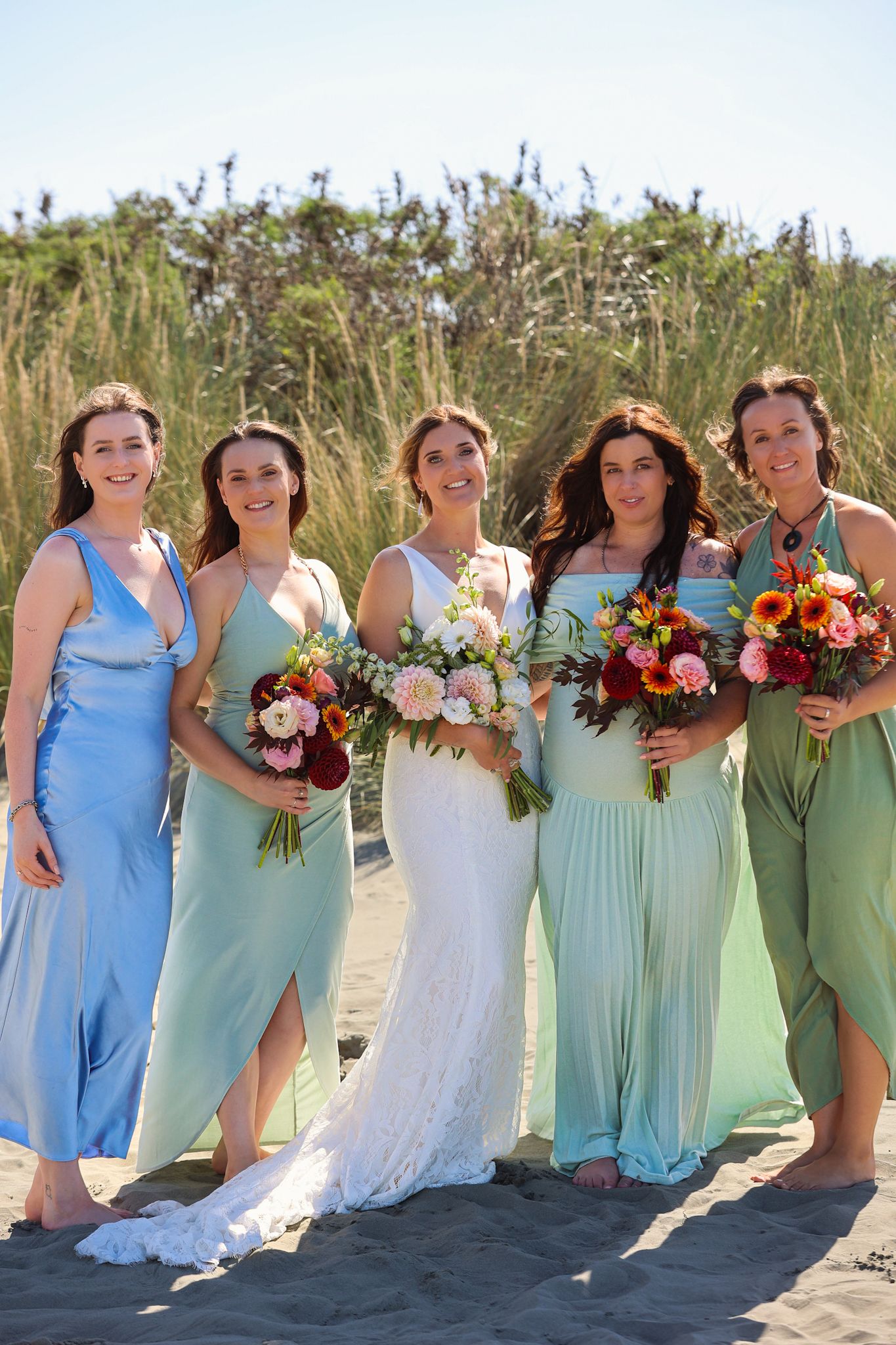 Bride and bridesmaids pose for a group photo in the sand