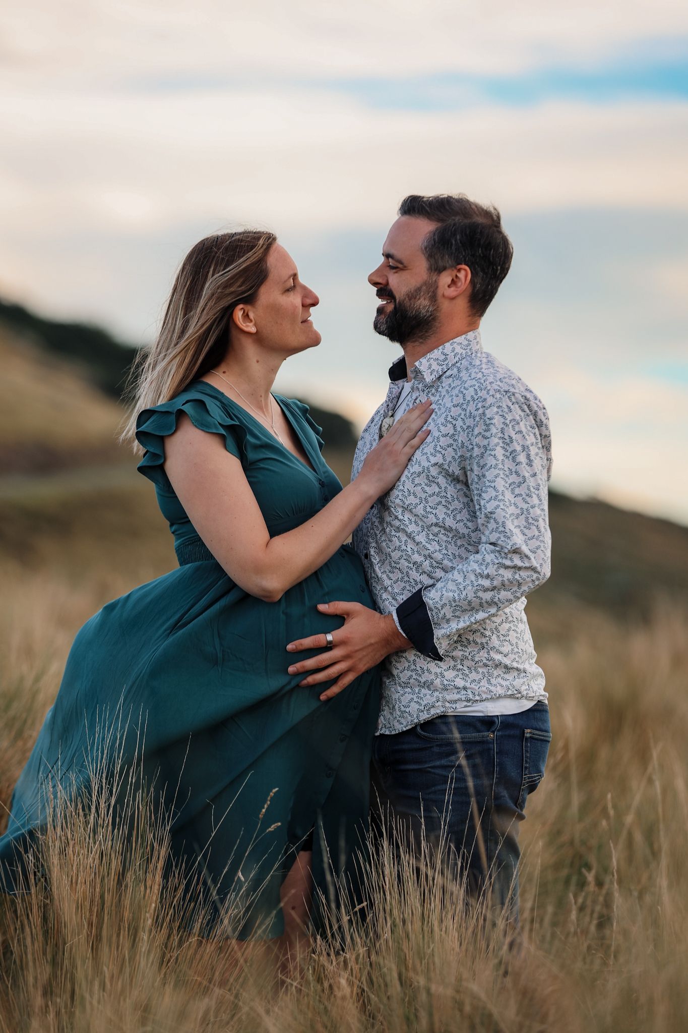 Expecting couple during a maternity photoshoot looking out onto christchurch city from the Port Hills, looking into each others eyes