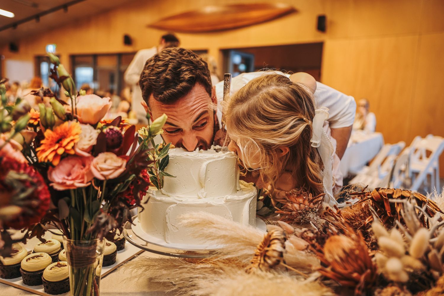 Groom and his daughter taking a big bite out of the whole cake after the initial cake cutting at a wedding