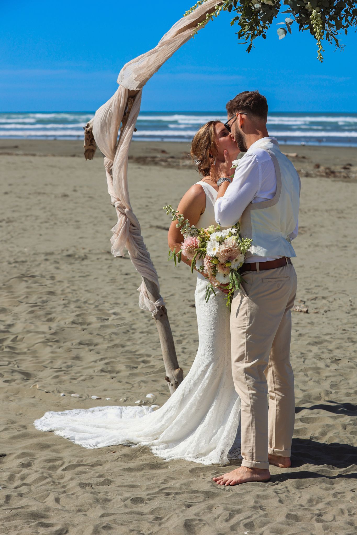 Newlyweds caught in their first kiss beneath a beachside wedding arch