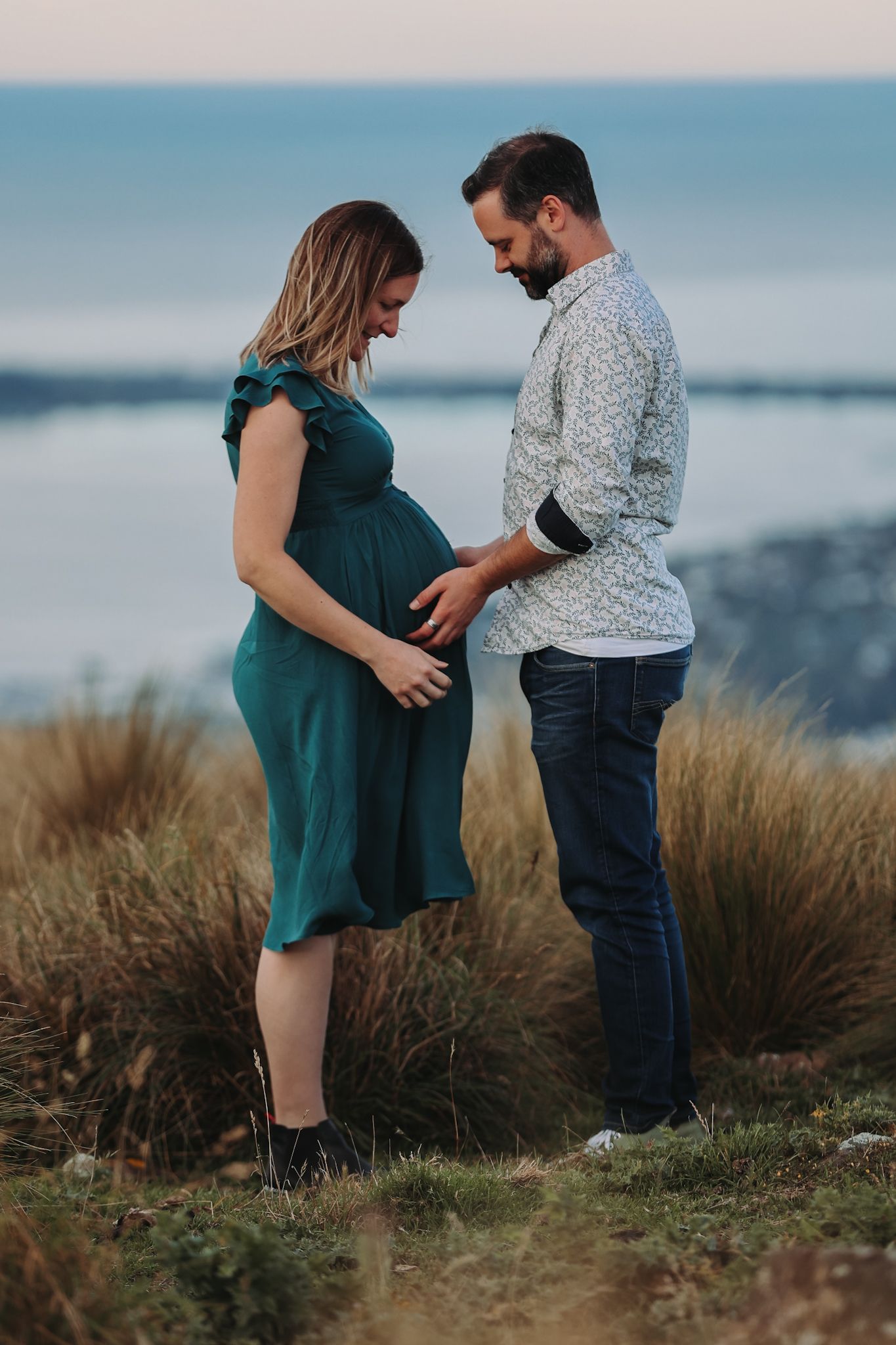 Expecting couple during a maternity photoshoot against a view of the ocean from the christchurch port hills.
