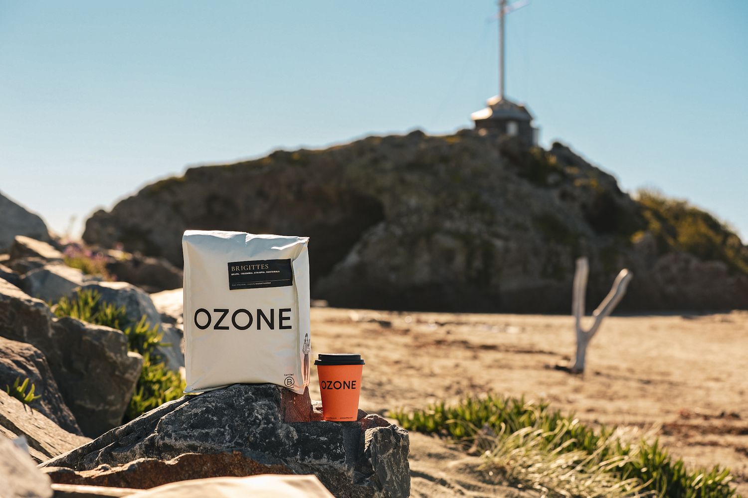 OZONE Coffee Roaster bean bad, decaf bag and coffee cups on Sumner Beach, Christchurch with cave rock in the background