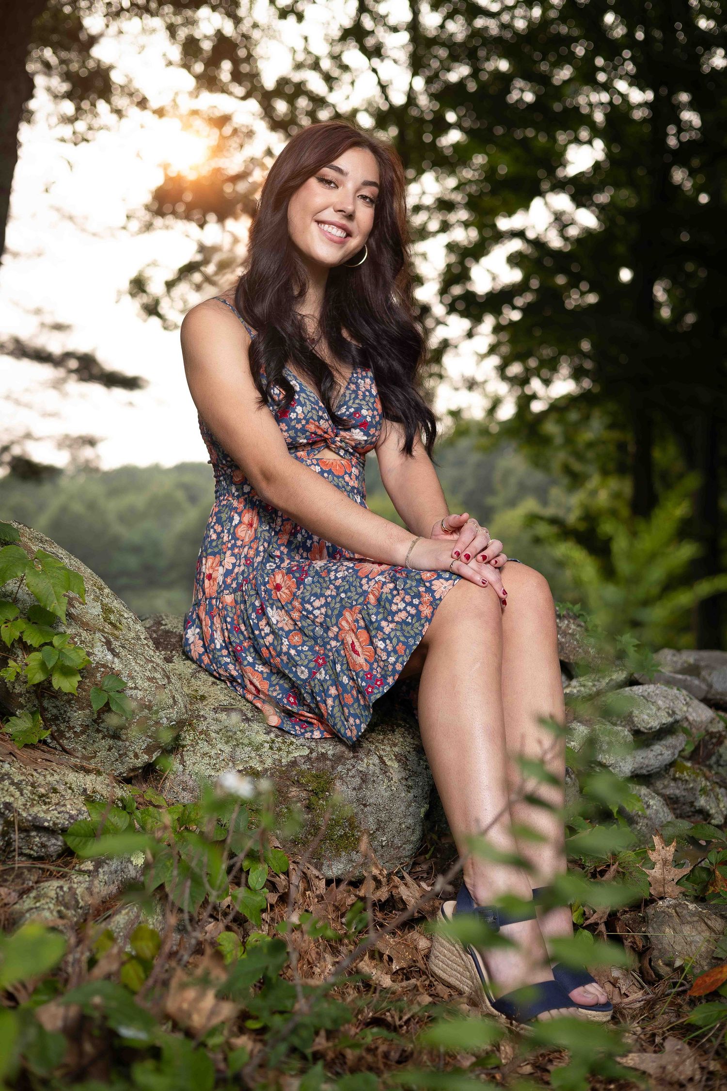 High school senior session of Libby sitting on a rock wall during sunset, beautiful lighting and warm smile.