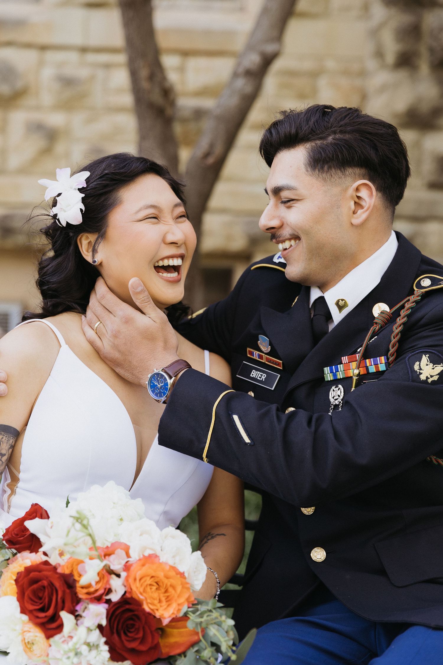 A joyful wedding moment with a military groom in dress uniform and bride sharing laughter outdoors.