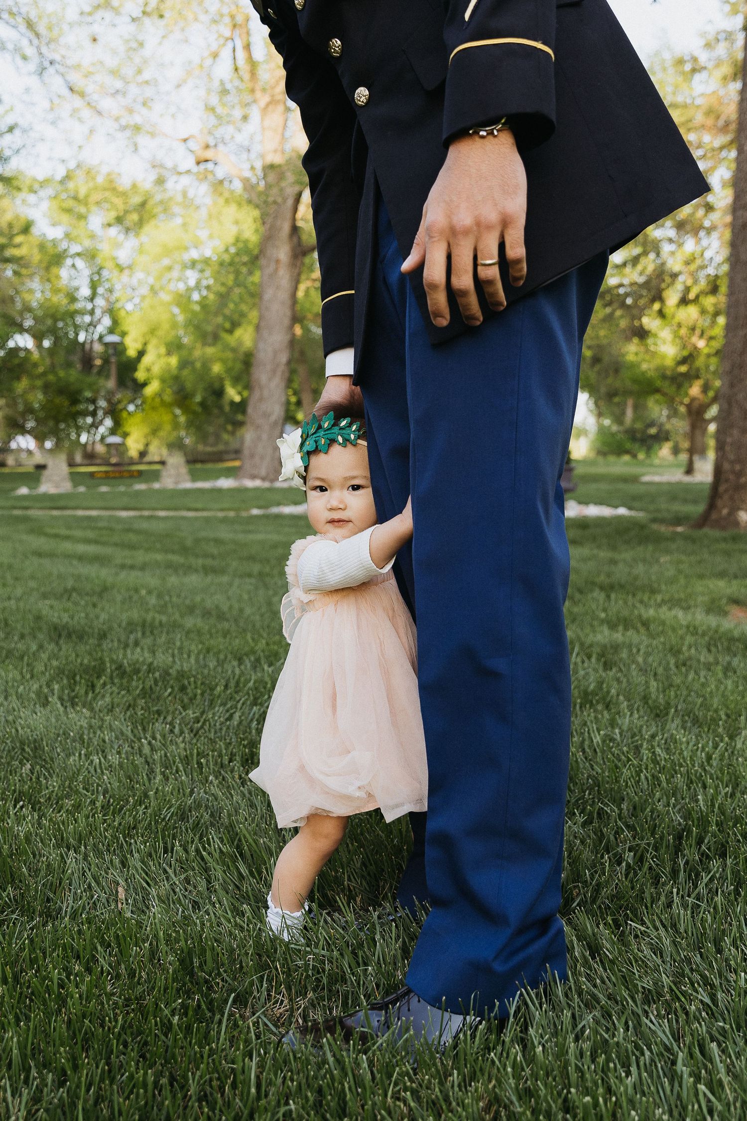 Small child in pink dress hugs the leg of someone in military dress uniform on grass.