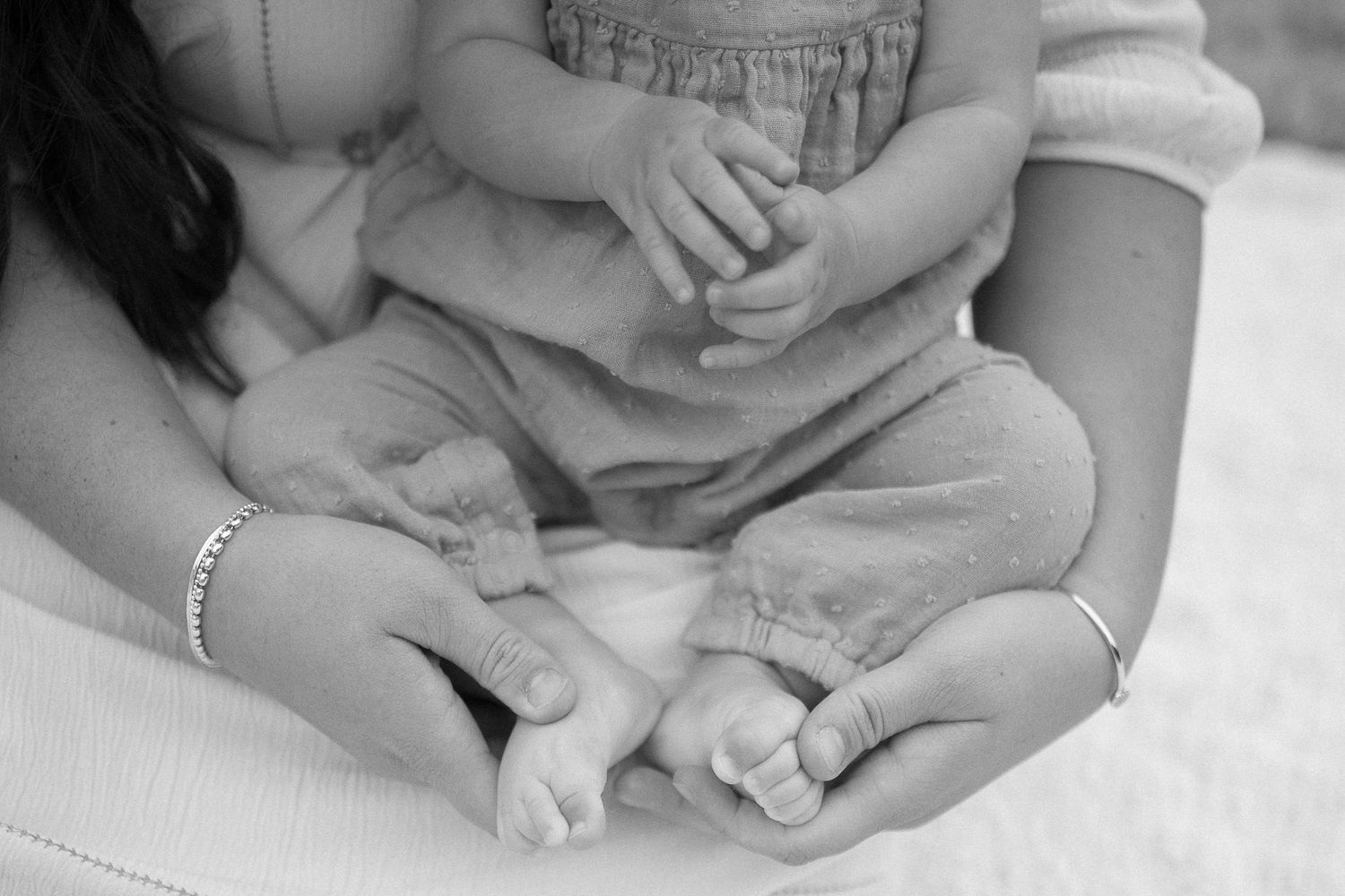 Close-up black and white image of parent and child's hands resting together.
