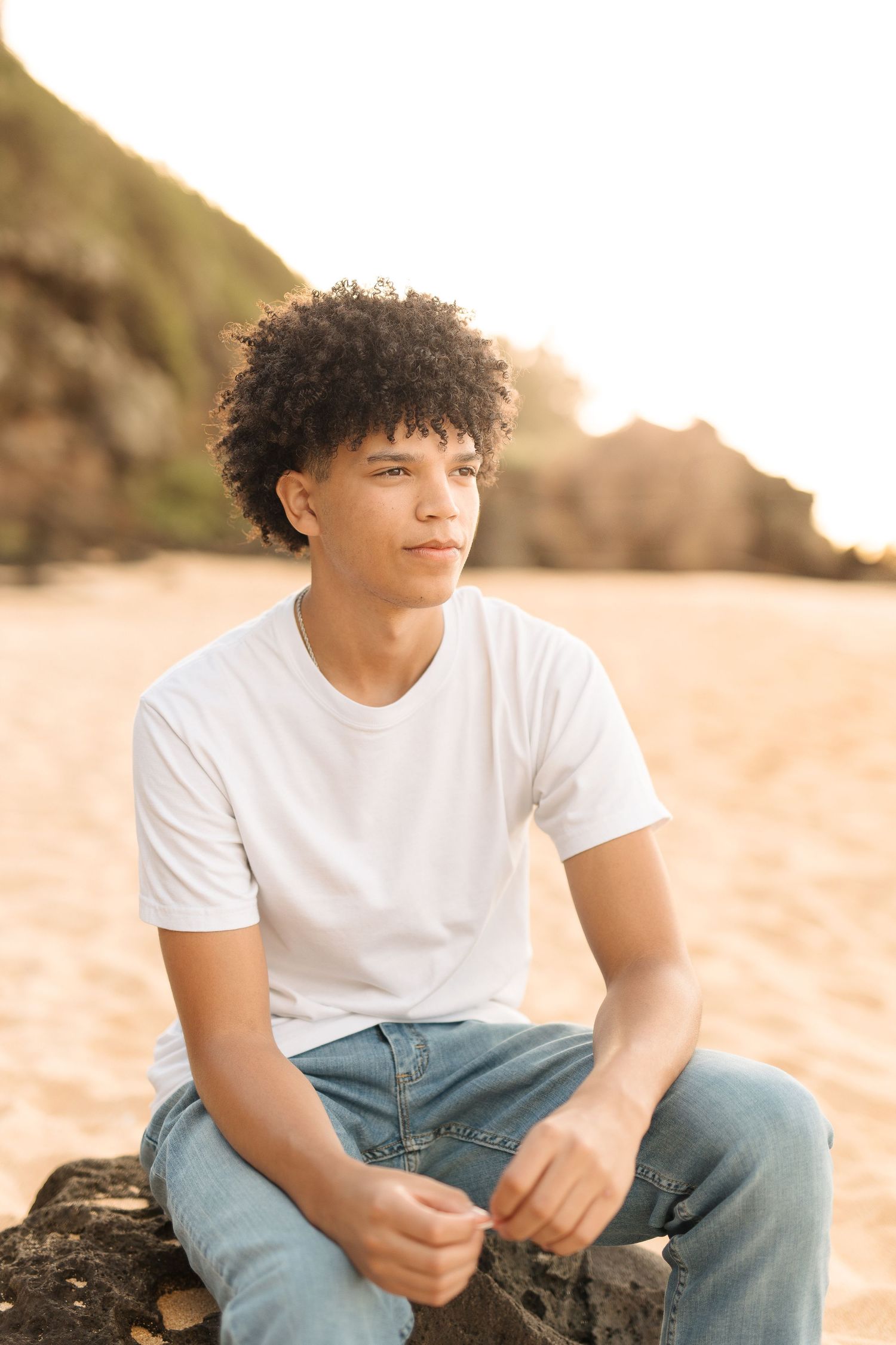 Portrait of person in casual white tee sitting thoughtfully on coastal rock. waimea bay senior session north shore oahu hawaii