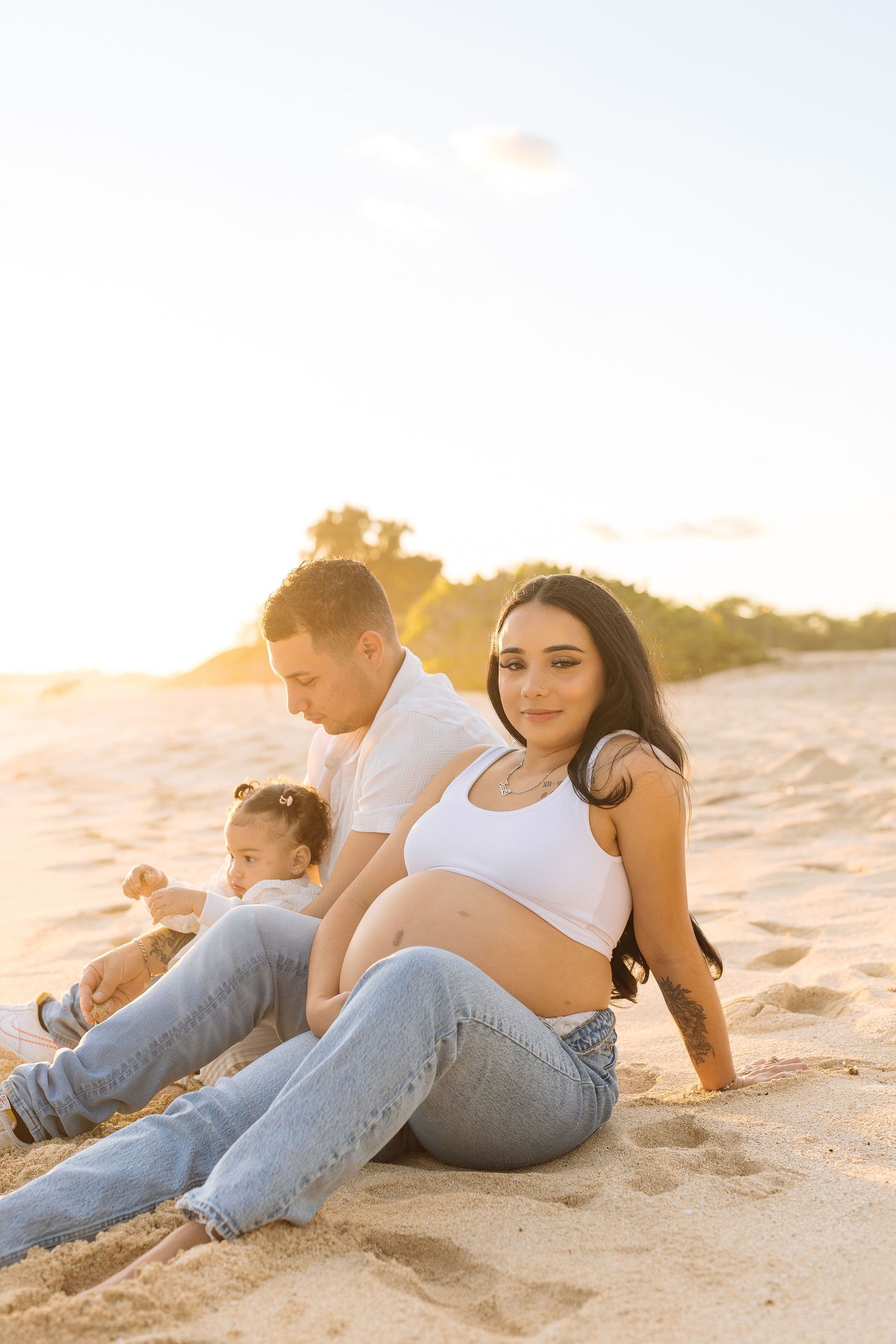 Family relaxes on sandy beach during golden hour sunset.