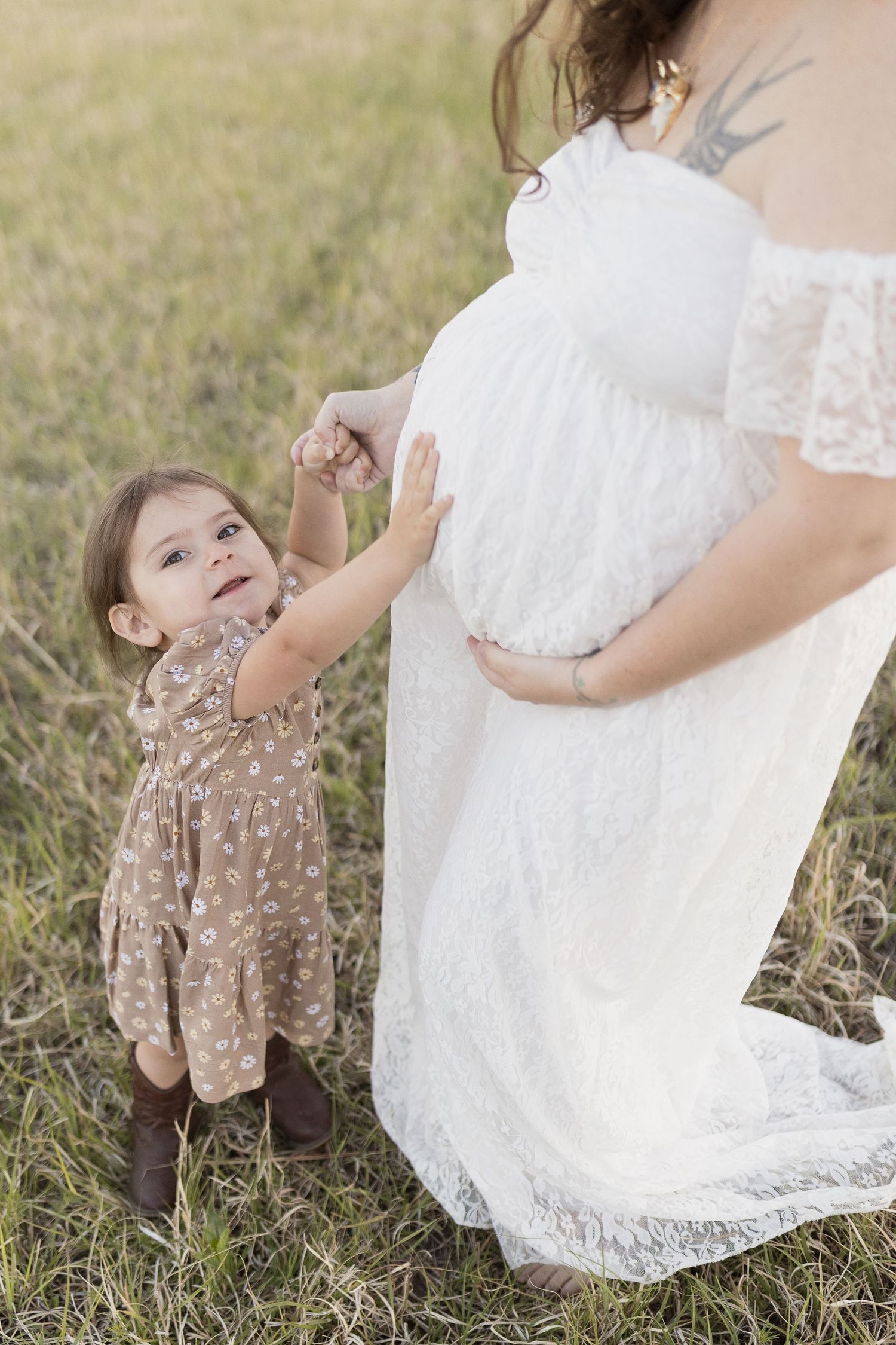 A sweet interaction between parent and child on grassy field during maternity photoshoot.