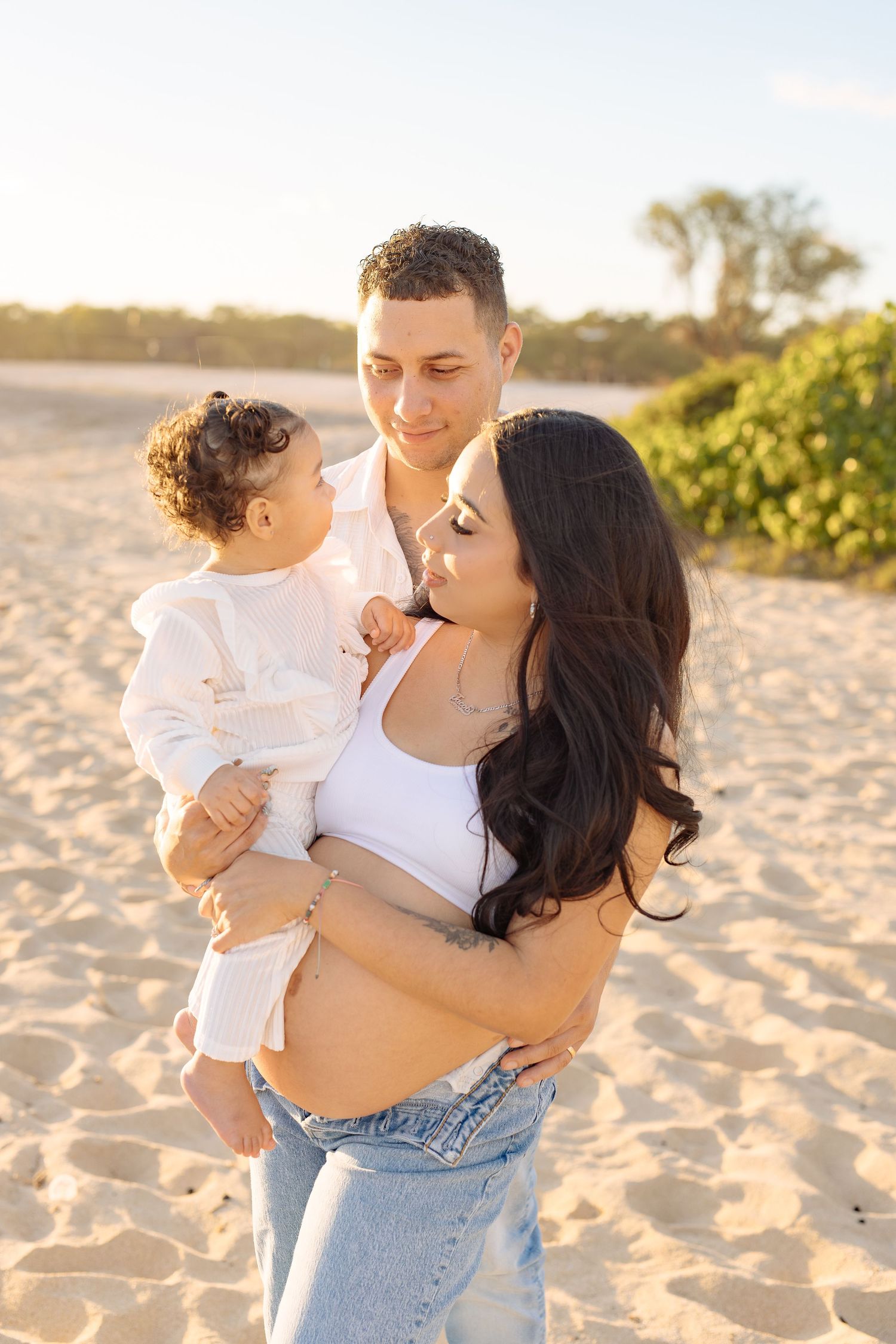 A family shares a tender moment on the beach during sunset in casual attire.