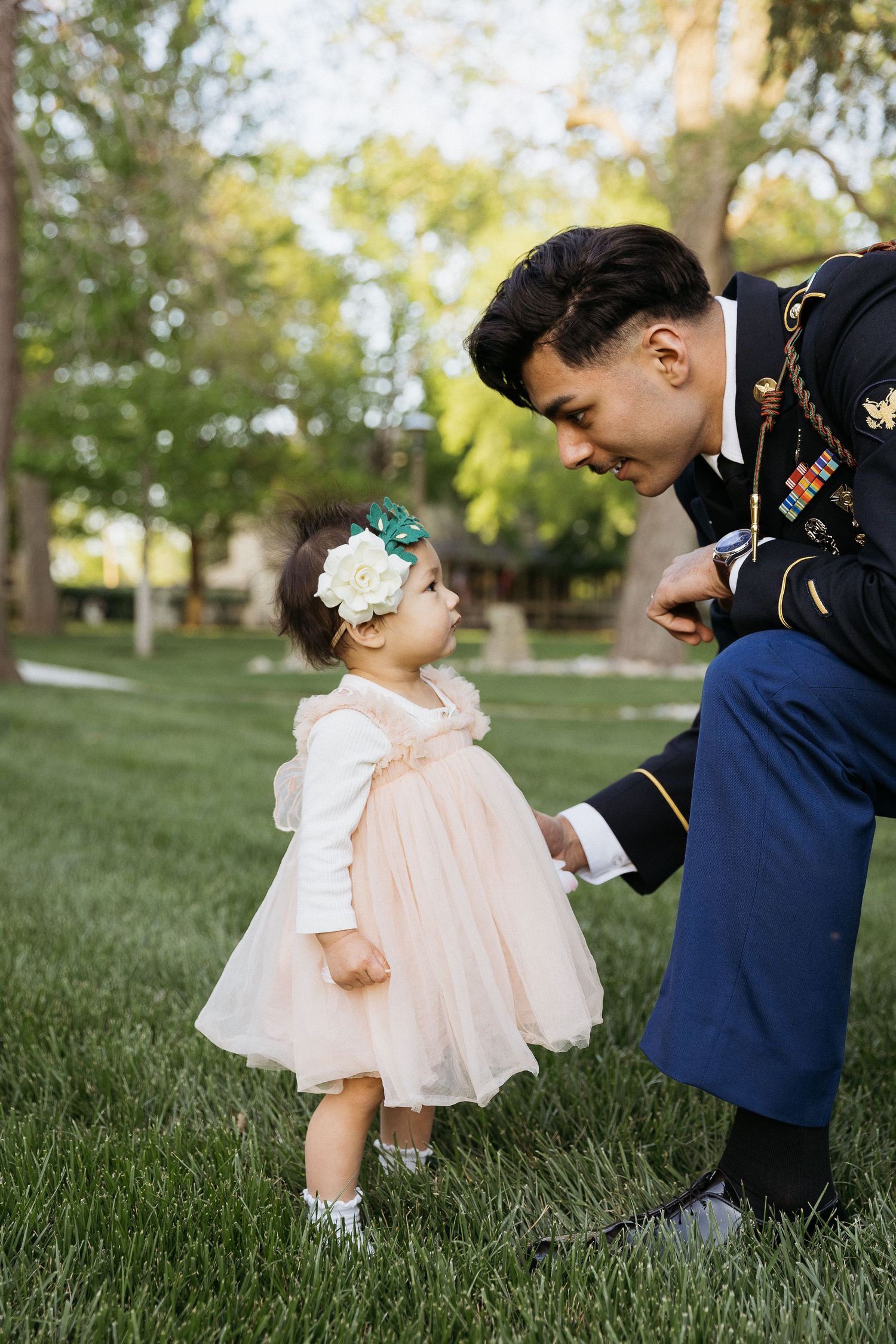 A sweet moment between military serviceman and toddler in pink dress on grass.