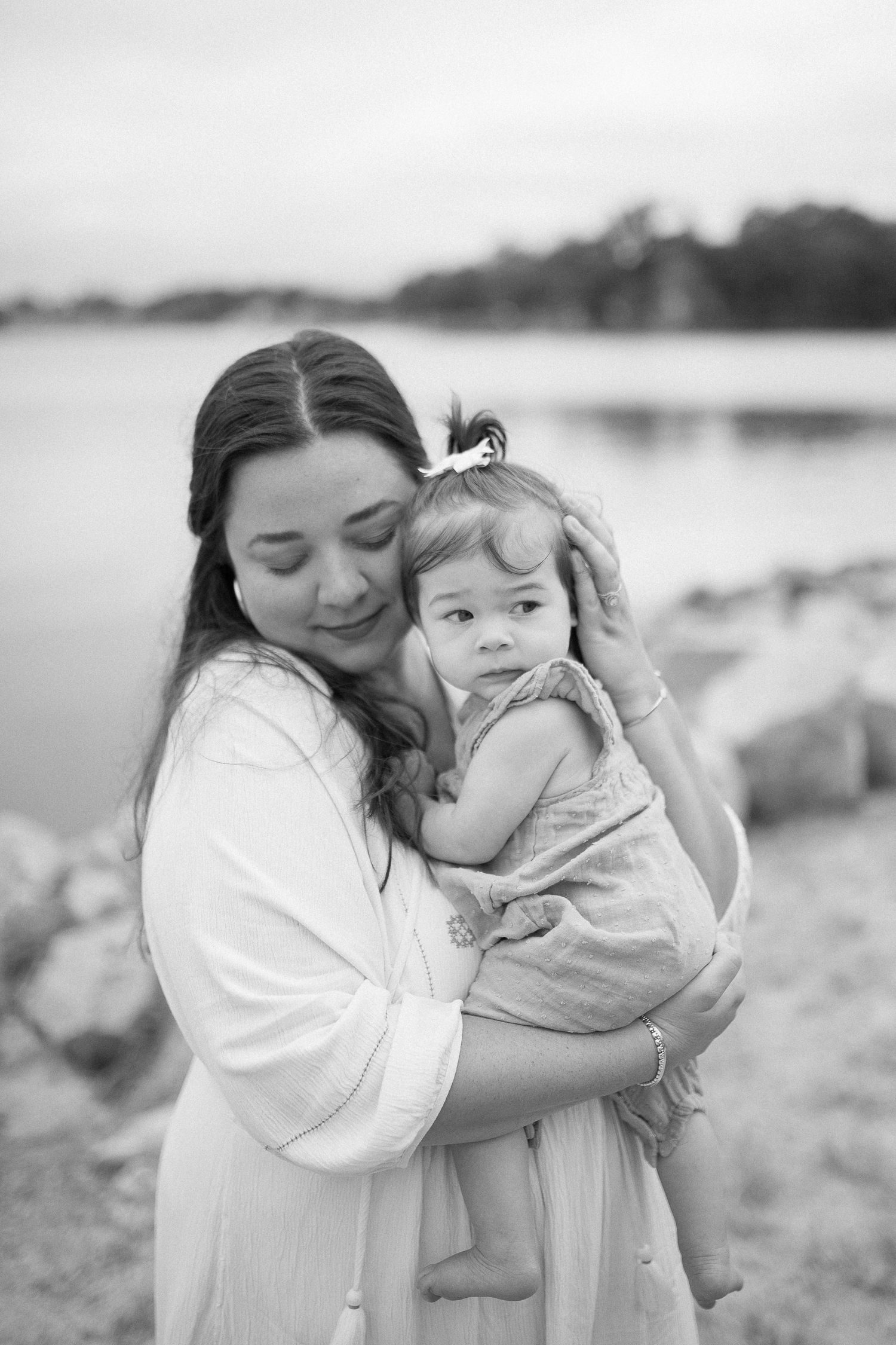 Black and white portrait of mother and child embracing by waterfront.