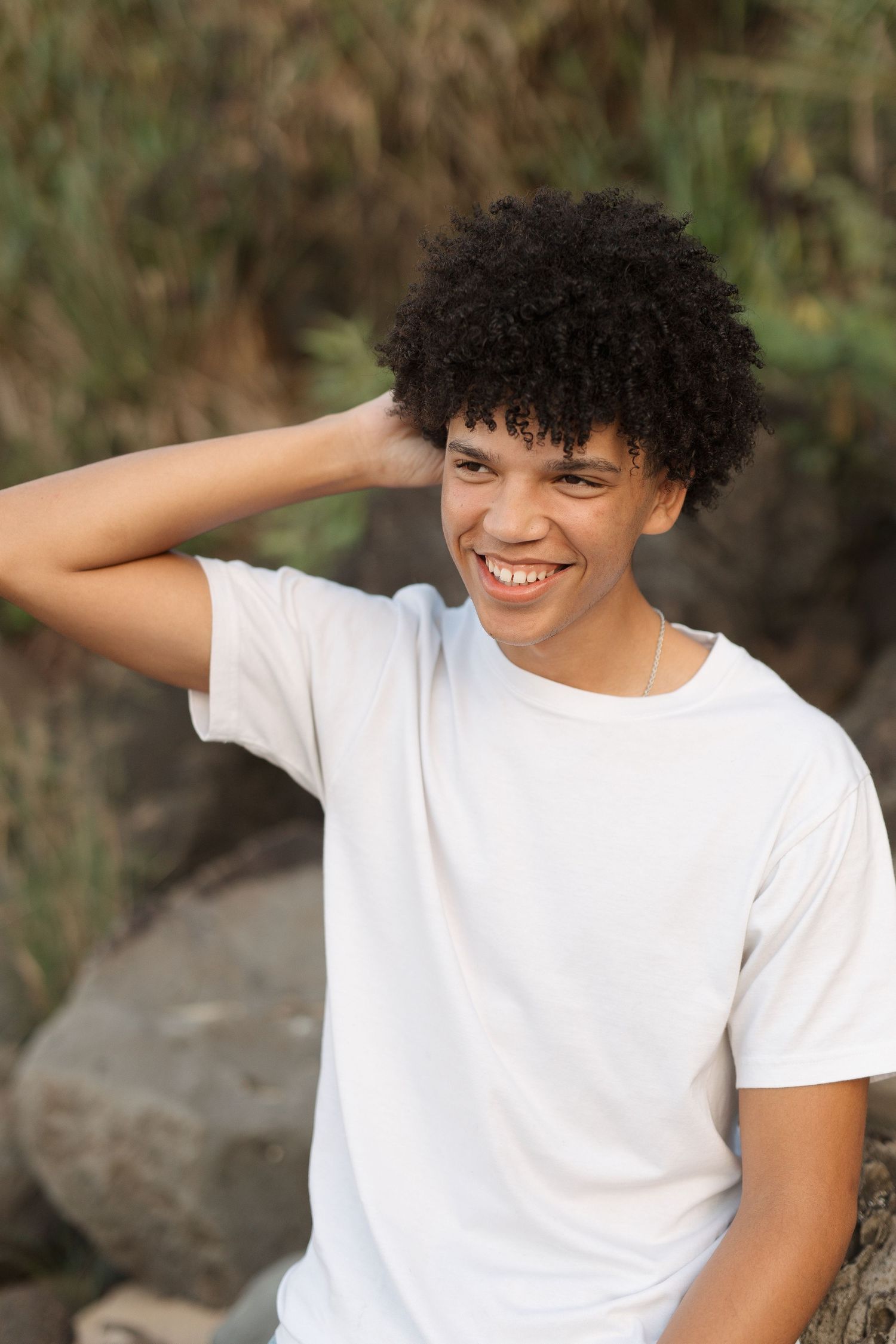 Candid outdoor portrait showing joyful expression while wearing white t-shirt against rock waimea bay senior session north shore