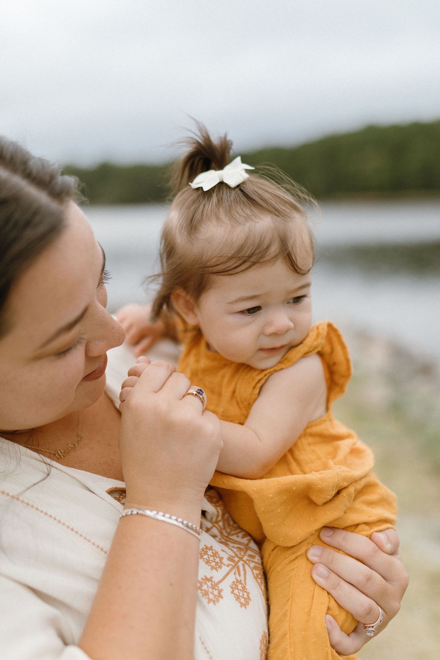 Tender moment between mother and child in white and orange outfits by the lake.
