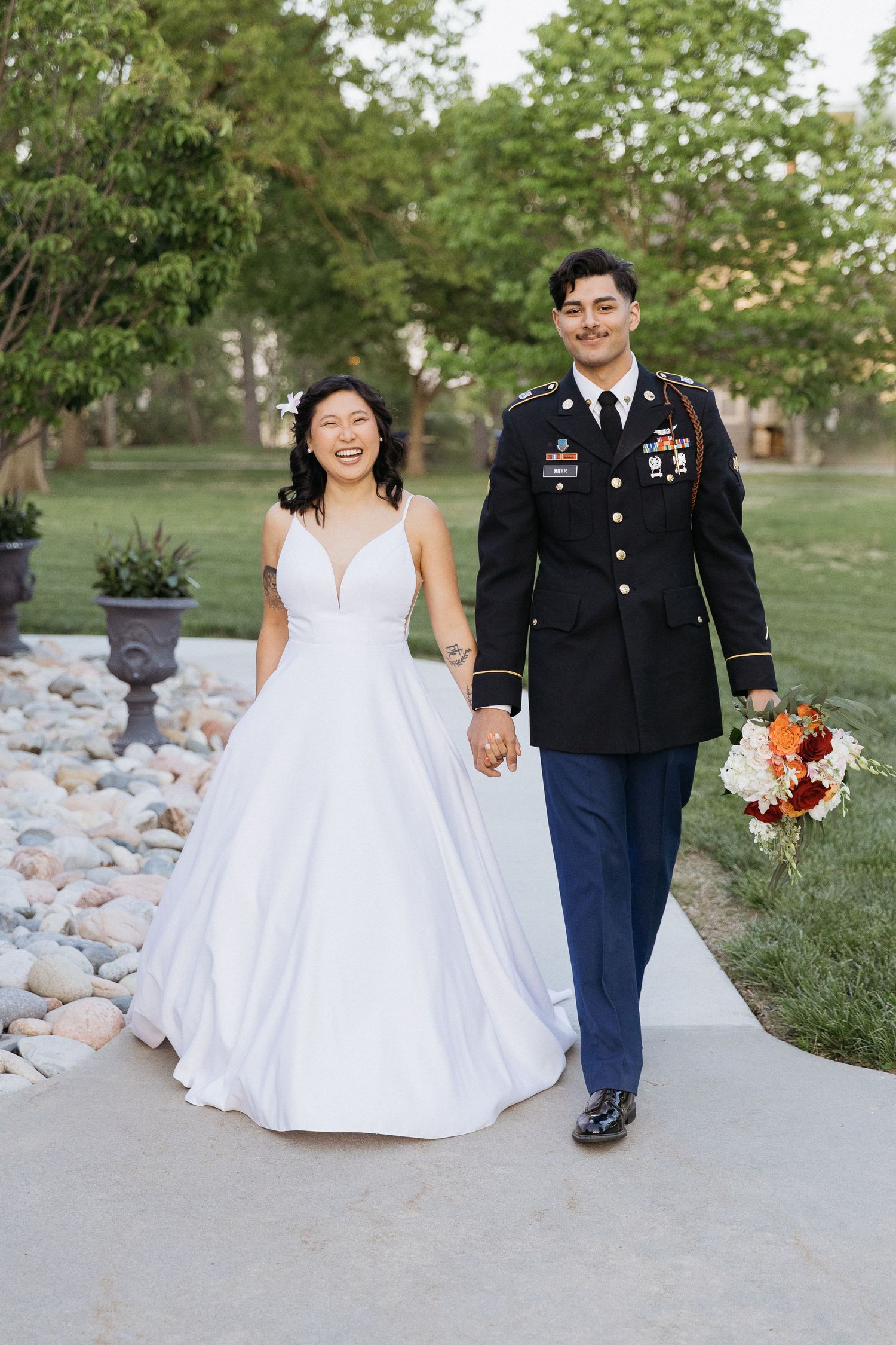 A wedding couple walking together on a path, with the bride in white and groom in military dress uniform.