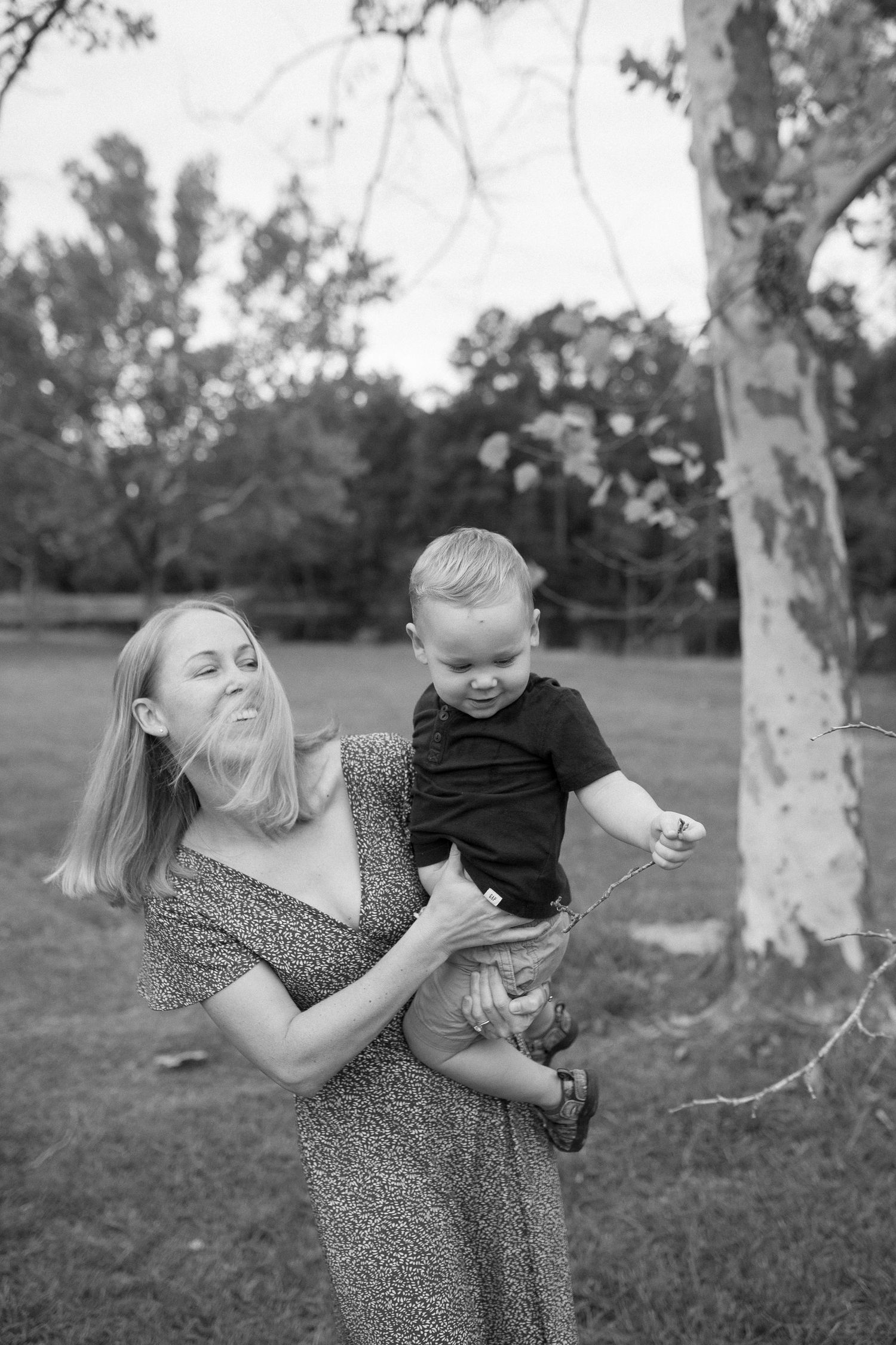 Playful black and white photograph of a mother and toddler sharing a joyful moment outdoors.