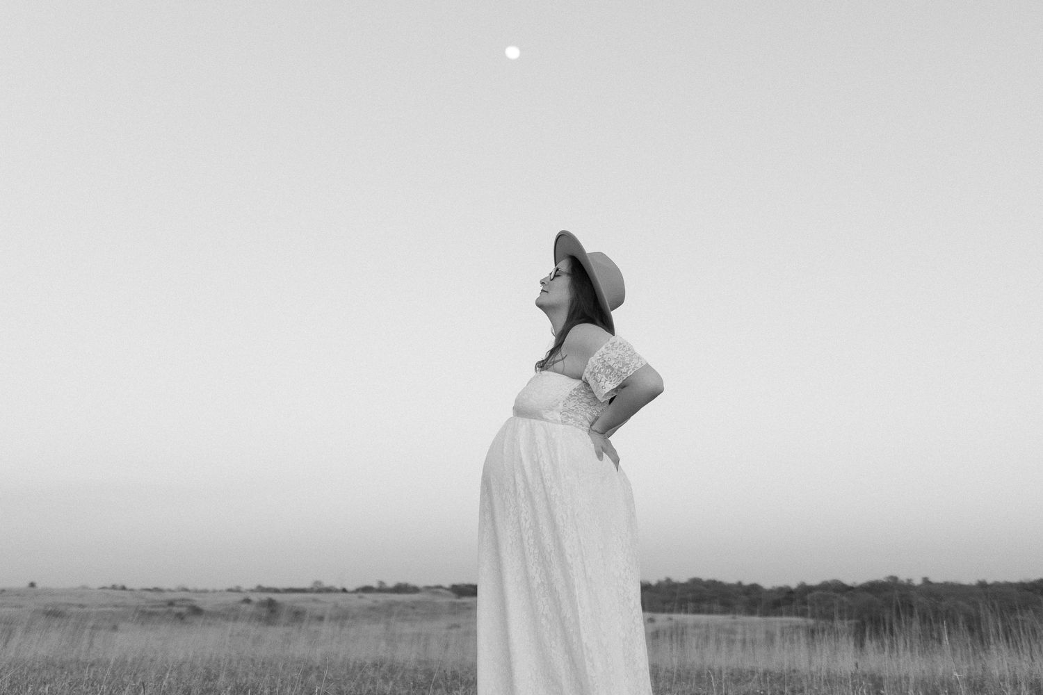 Black and white silhouette of expecting mother in prairie field at dusk.
