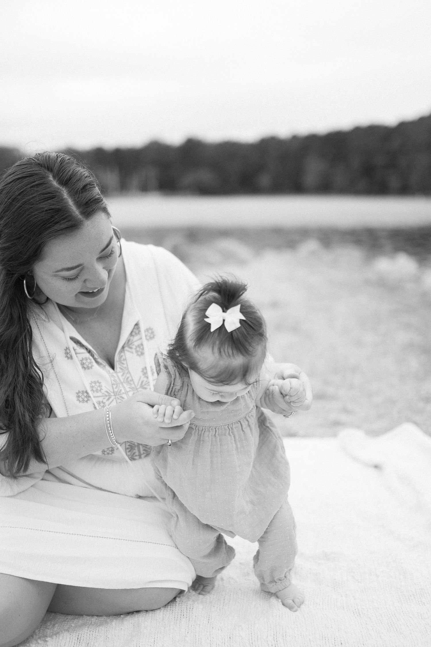 Black and white photo of tender moment between parent and child on blanket by lake.