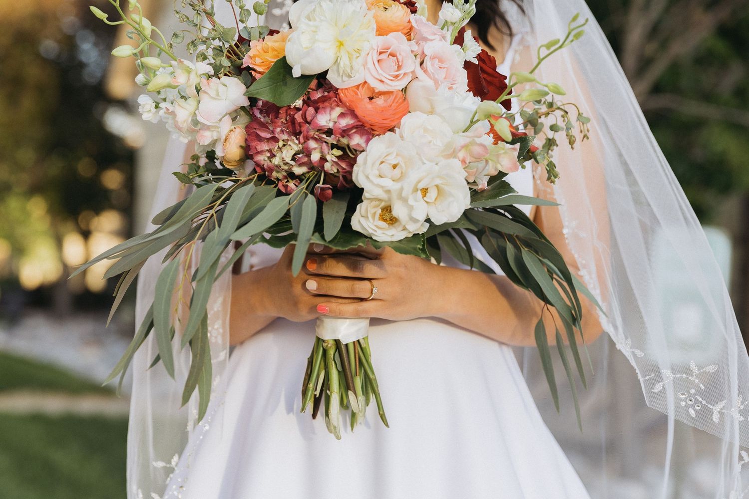 Bridal bouquet with peach and white roses wrapped in white ribbon against wedding dress.